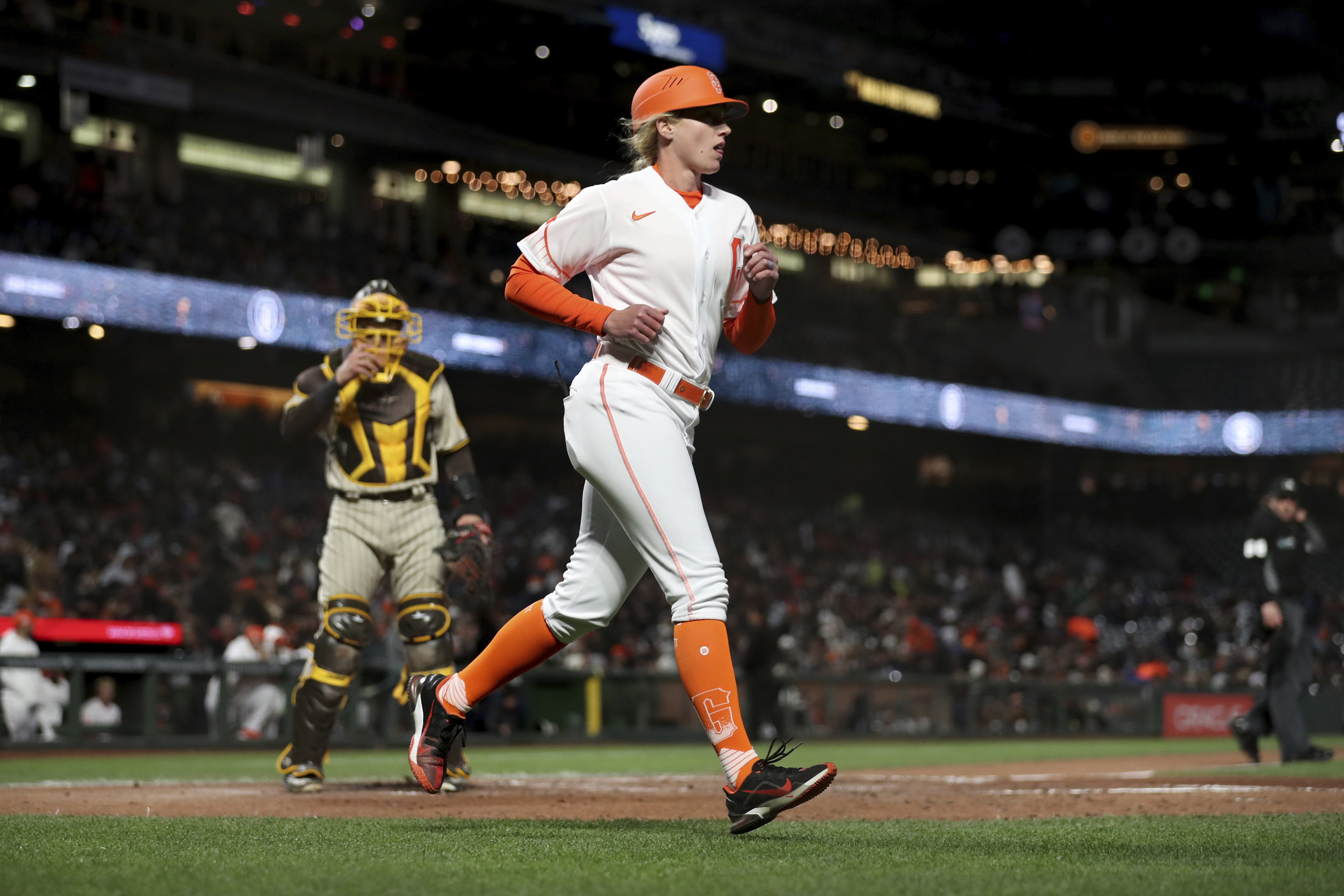 San Francisco Giants first base coach Alyssa Nakken runs to get in position, near San Diego Padres catcher Austin Nola, left, during the third inning of a baseball game in San Francisco, Tuesday, April 12, 2022. 