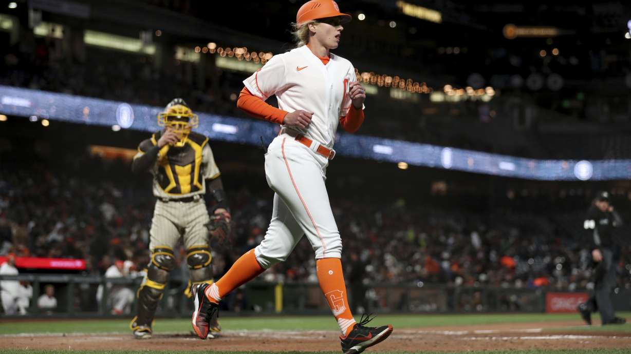 San Francisco Giants first base coach Alyssa Nakken runs to get in position, near San Diego Padres catcher Austin Nola, left, during the third inning of a baseball game in San Francisco, Tuesday, April 12, 2022.