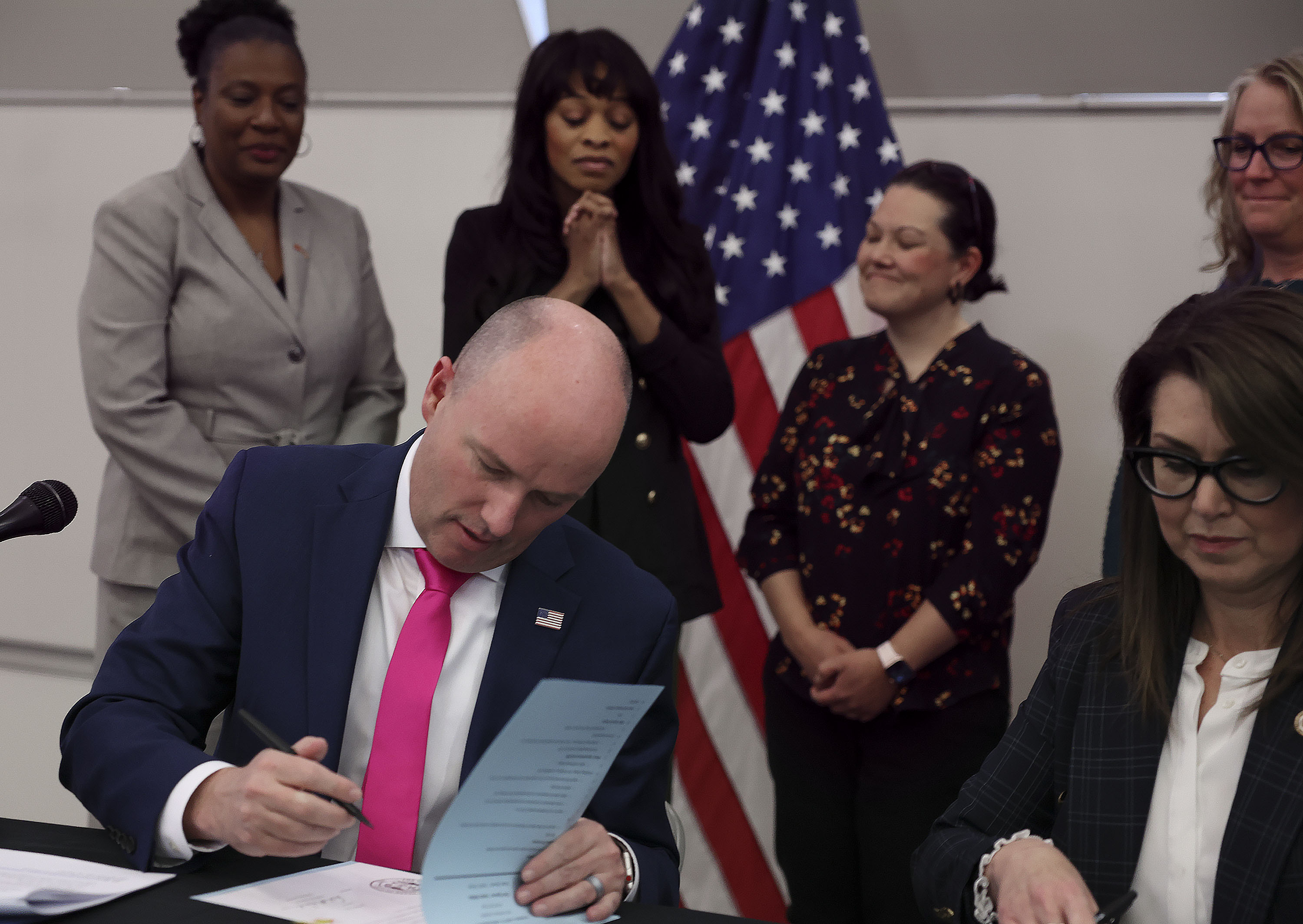 Brittany Tichenor-Cox, mother of Isabella “Izzy” Tichenor, second from left, watches as Gov. Spencer Cox signs HB428, sponsored by Rep. Sandra Hollins, D-Salt Lake City, left, during a ceremonial signing of bills focused on educational issues at Hillcrest Junior High in Murray on Thursday.
