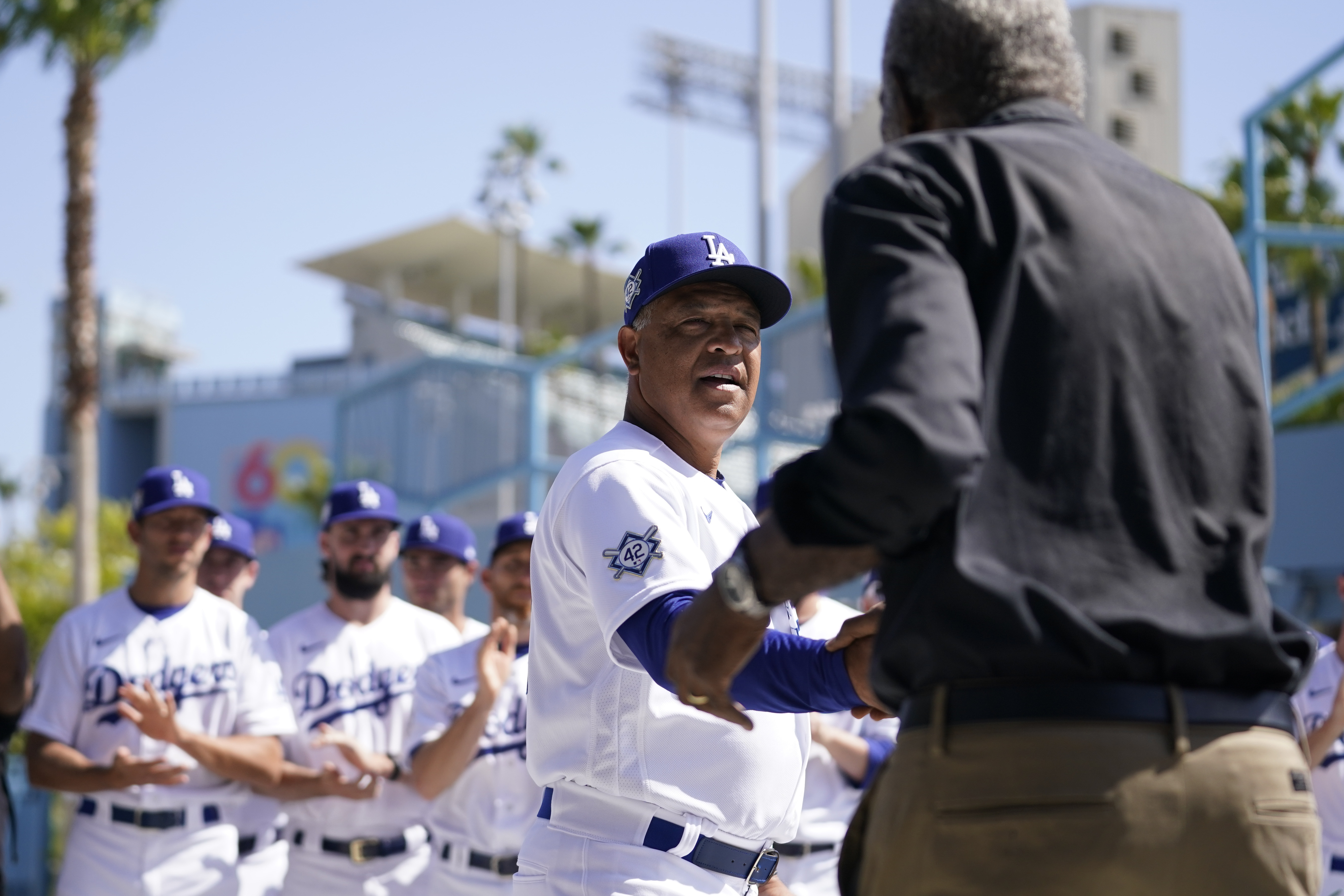 Los Angeles Dodgers' manager Dave Roberts, center, shakes hands with David Robinson, son of Jackie Robinson, before a baseball game between the Cincinnati Reds and the Los Angeles Dodgers in Los Angeles, Friday, April 15, 2022. Today MLB celebrates Jackie Robinson Day, in honor of Robinson, who was the first African American to play in the major leagues.