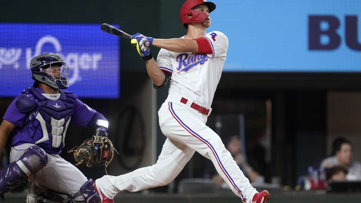 Texas Rangers' Corey Seager flies out to center, next to Colorado Rockies catcher Elias Diaz during the fifth inning of a baseball game Tuesday, April 12, 2022, in Arlington, Texas.