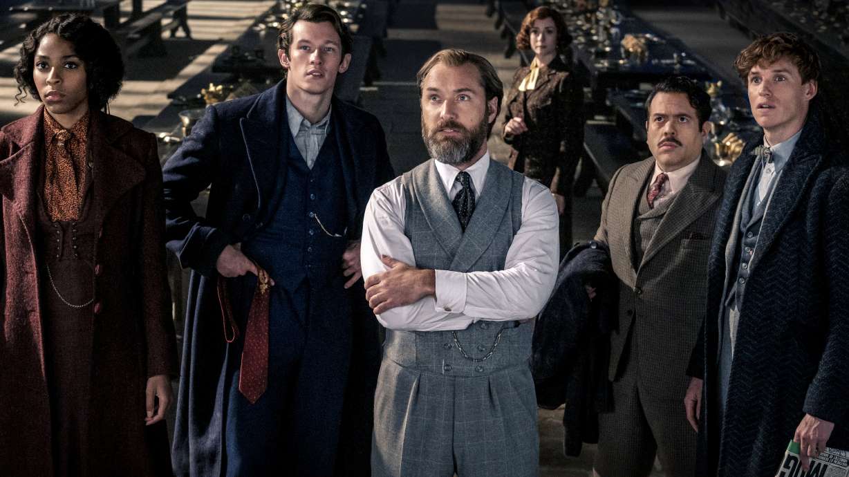 This image released by Warner Bros. Pictures shows, from left, Jessica Williams, Callum Turner, Jude Law, Fionna Glascott, Dan Fogler and Eddie Redmayne in a scene from "Fantastic Beasts: The Secrets of Dumbledore."