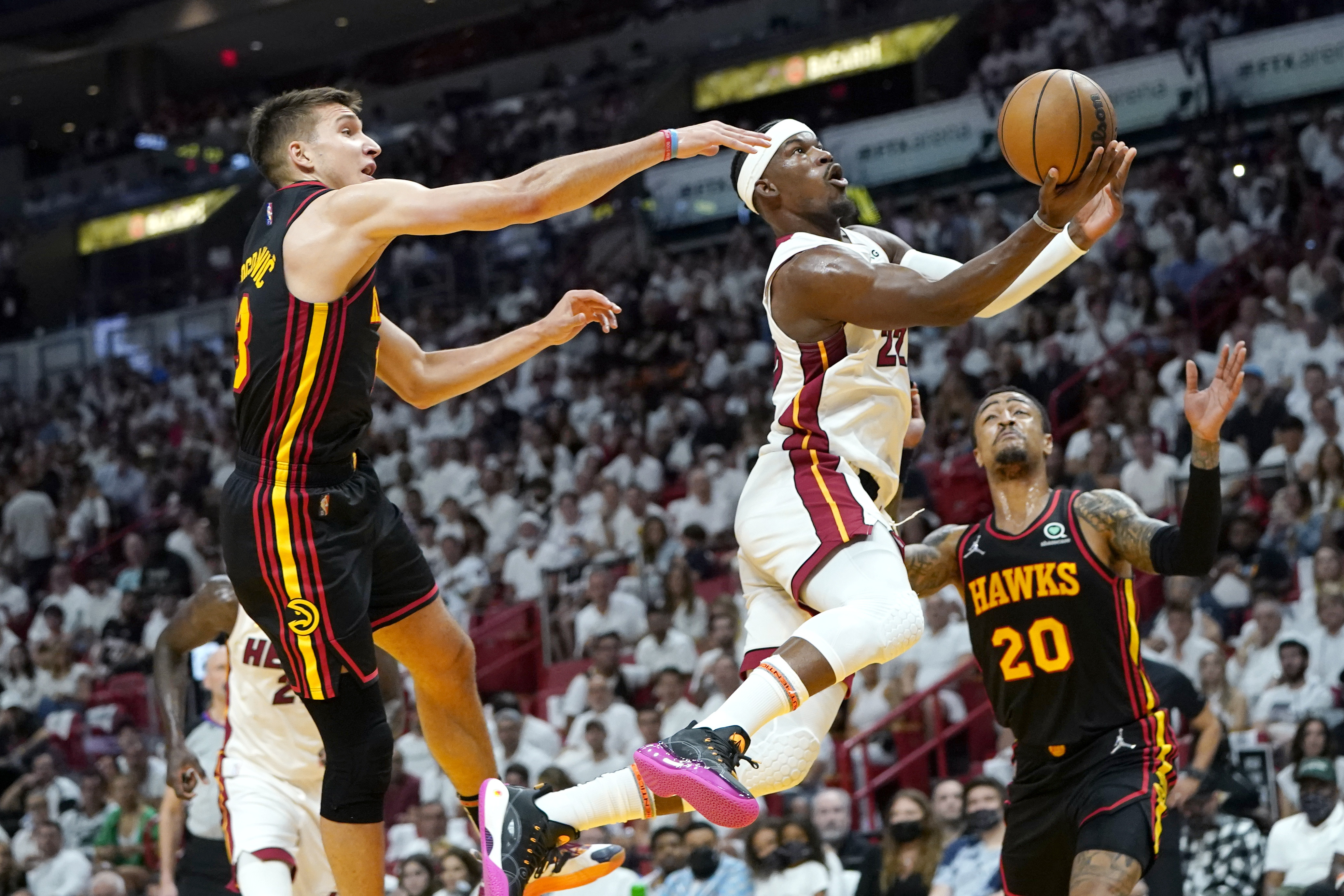 Miami Heat forward Jimmy Butler (22) goes to the basket as Atlanta Hawks guard Bogdan Bogdanovic, left, and forward John Collins (20) defend during the first half of Game 1 of an NBA basketball first-round playoff series, Sunday, April 17, 2022, in Miami. 