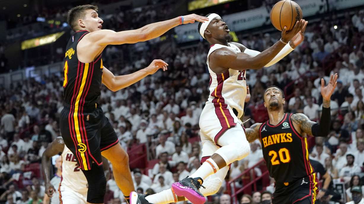 Miami Heat forward Jimmy Butler (22) goes to the basket as Atlanta Hawks guard Bogdan Bogdanovic, left, and forward John Collins (20) defend during the first half of Game 1 of an NBA basketball first-round playoff series, Sunday, April 17, 2022, in Miami.