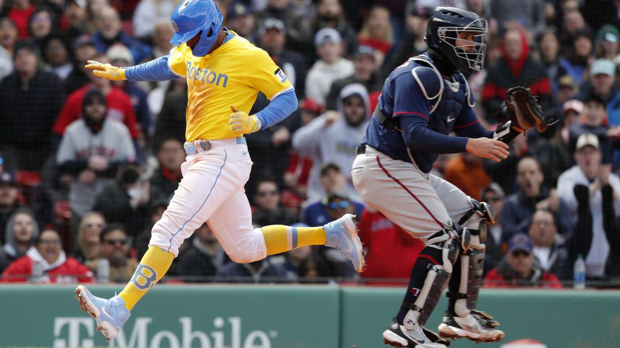 Boston Red Sox's Xander Bogaerts, left, scores behind Minnesota Twins' Gary Sanchez on a sacrifice fly by Alex Verdugo during the sixth inning of a baseball game, Sunday, April 17, 2022, in Boston.