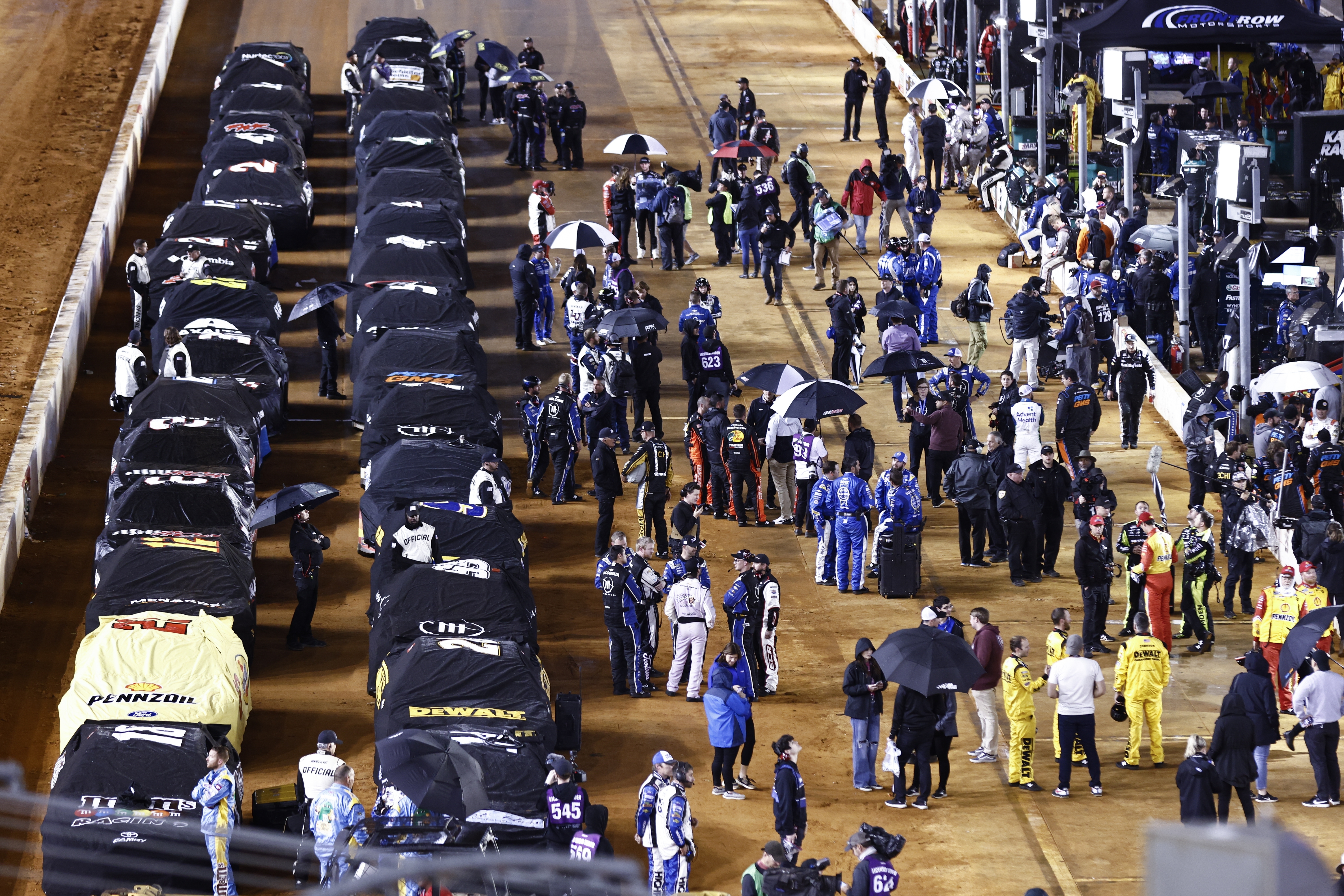 Cars sit under covers and drivers stand along side of them on pit road during a rain delay in a NASCAR Cup Series auto race, late Sunday, April 17, 2022, in Bristol, Tenn. 