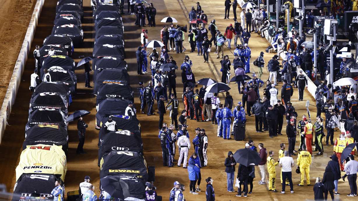 Cars sit under covers and drivers stand along side of them on pit road during a rain delay in a NASCAR Cup Series auto race, late Sunday, April 17, 2022, in Bristol, Tenn.