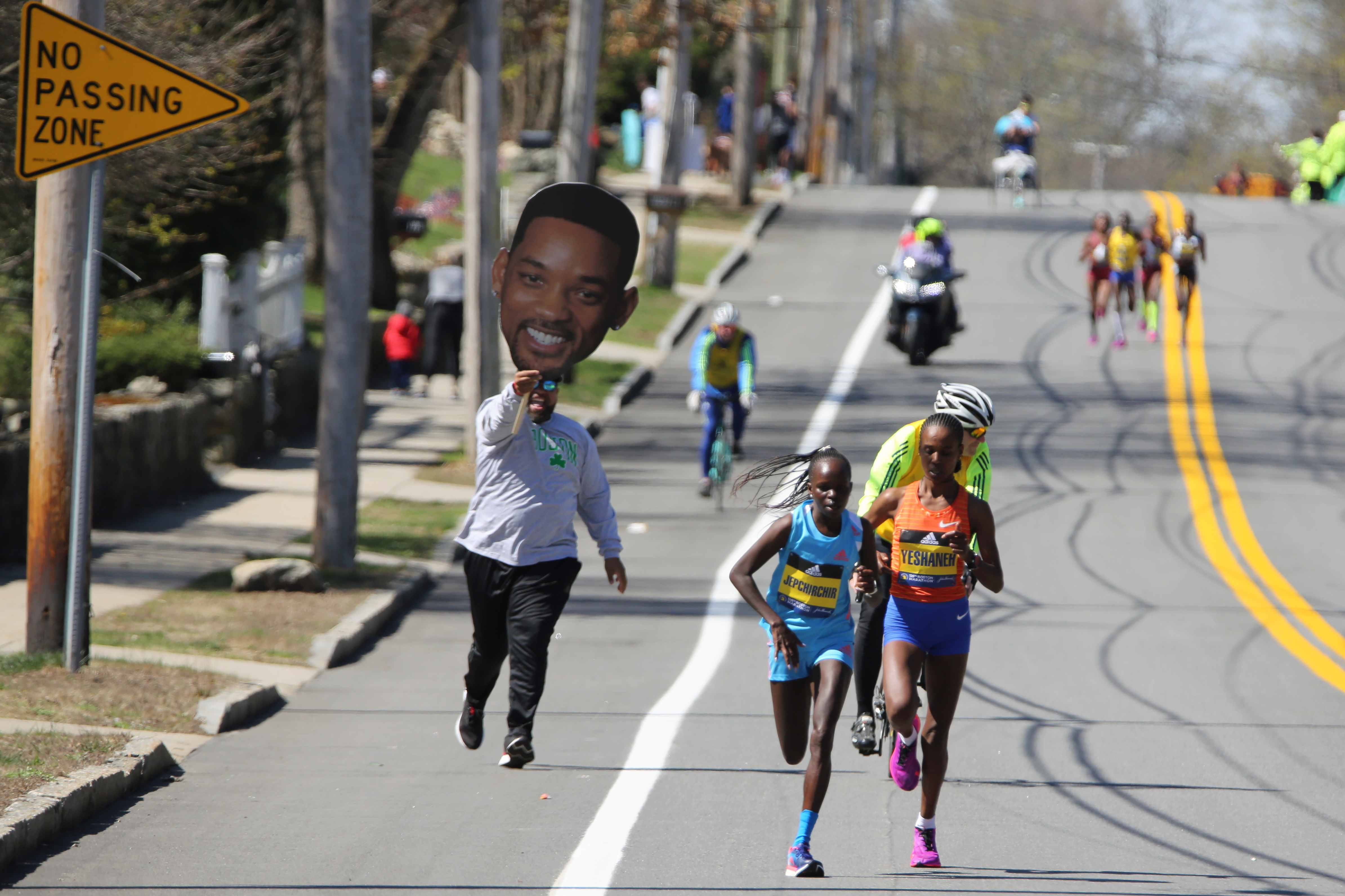 A man carrying a picture of actor Will Smith runs behind Peres Jepchirchir, of Kenya, left, and Ababel Yeshaneh, of Ethiopia, during the 126th Boston Marathon in Natick, Mass, Monday, April 18, 2022. 