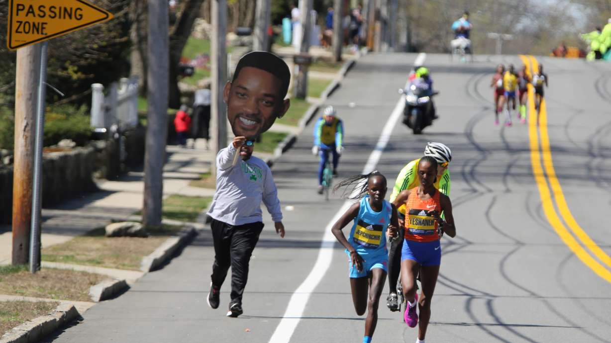A man carrying a picture of actor Will Smith runs behind Peres Jepchirchir, of Kenya, left, and Ababel Yeshaneh, of Ethiopia, during the 126th Boston Marathon in Natick, Mass, Monday, April 18, 2022.