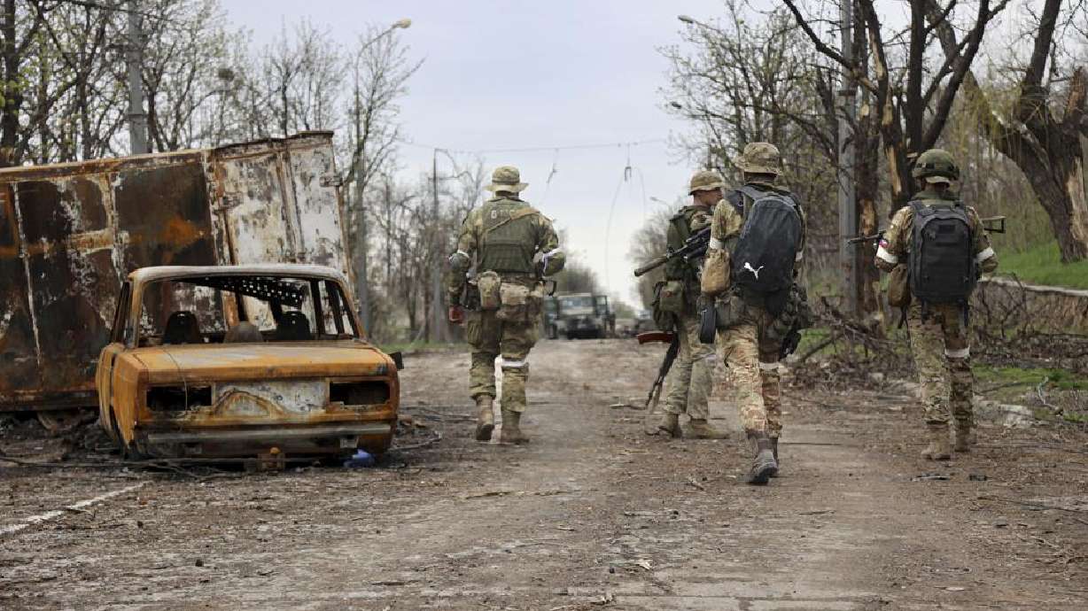 Servicemen of Donetsk People's Republic militia walk past damaged vehicles in Mariupol, Ukraine, Tuesday. Russia taking Mariupol would deprive Ukraine of a vital port and complete a land bridge between Russia and the Crimean Peninsula.