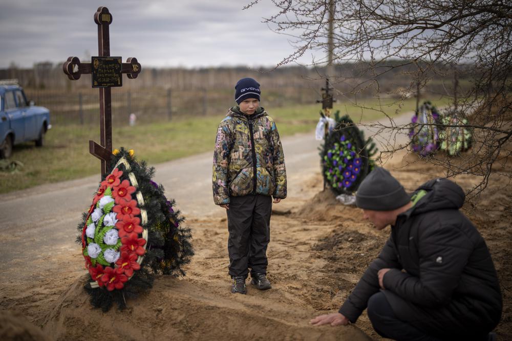 Vova, 10, looks at the grave of his mother, Maryna, while his father, Ivan Drahun, prays during her funeral in Bucha, on the outskirts of Kyiv, Ukraine, on Wednesday. Vova's mother died while they were sheltered in a cold basement for more than a month during the Russian military's occupation.