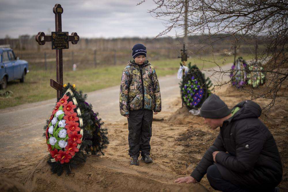Vova, 10, looks at the grave of his mother, Maryna, while his father, Ivan Drahun, prays during her funeral in Bucha, on the outskirts of Kyiv, Ukraine, on Wednesday. Vova's mother died while they were sheltered in a cold basement for more than a month during the Russian military's occupation.