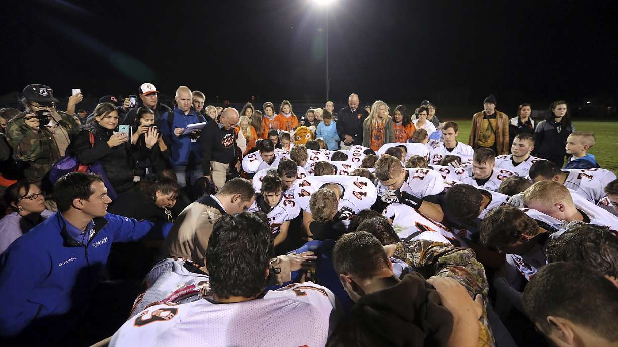 FILE - Bremerton assistant football coach Joe Kennedy, obscured at center in blue, is surrounded by Centralia High School football players as they kneel and pray with him on the field after their game against Bremerton on Oct. 16, 2015, in Bremerton, Wash. After losing his coaching job for refusing to stop kneeling in prayer with players and spectators on the field immediately after football games, Kennedy will take his arguments before the U.S. Supreme Court on Monday, April 25, 2022, saying the Bremerton School District violated his First Amendment rights by refusing to let him continue praying at midfield after games.