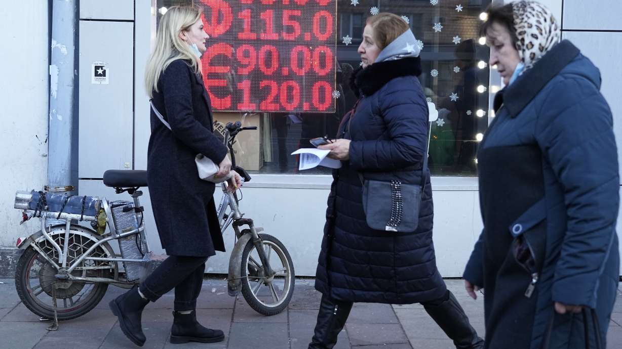 People walk past a currency exchange office screen displaying the exchange rates of U.S. Dollar and Euro to Russian Rubles in Moscow's downtown, Russia. Nearly two months into the Russian-Ukraine war, the Kremlin has taken extraordinary steps to blunt an economic counteroffensive from the West.
