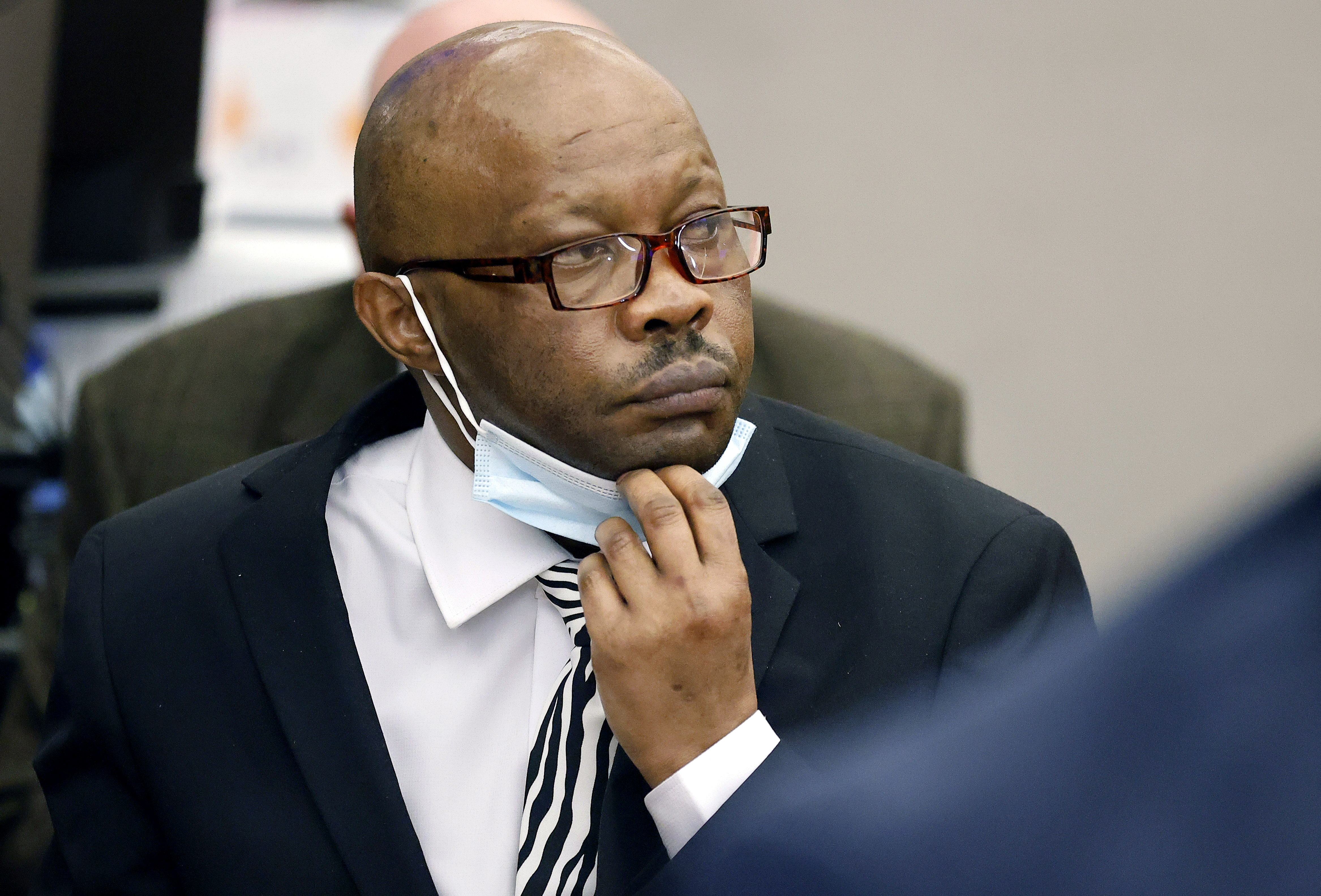 Defendant Billy Chemirmir lowers his mask as a state witness is asked to identify him during his murder trial at the Frank Crowley Courts Building in Dallas, Nov. 17, 2021. The retrial of the man charged with killing 18 older women in the Dallas area over a two-year span is set to begin Monday, after the first jury to hear a case against him deadlocked. 