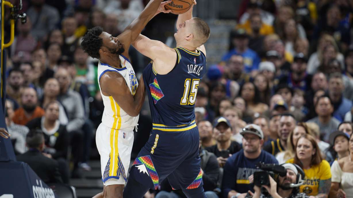 Golden State Warriors forward Andrew Wiggins, left, blocks a shot by Denver Nuggets center Nikola Jokic in the first half of Game 4 of an NBA basketball first-round Western Conference playoff series Sunday, April 24, 2022, in Denver.