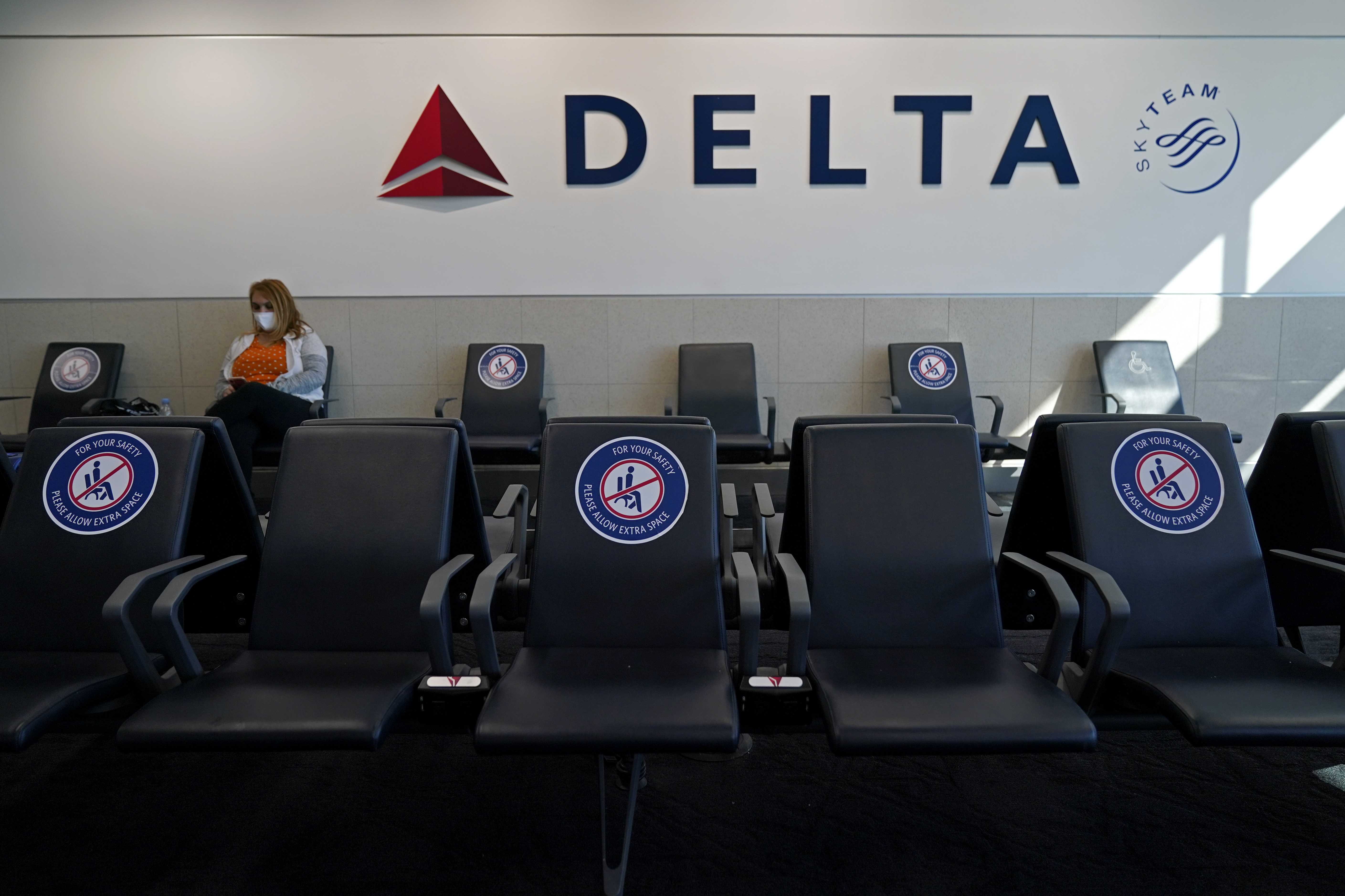 A passenger wears a face mask as she waits in a socially-distance area for a Delta Airlines flight, Feb. 3, 2021, at Hartsfield-Jackson International Airport in Atlanta. Delta Air Lines will start paying flight attendants during the time that passengers are boarding.