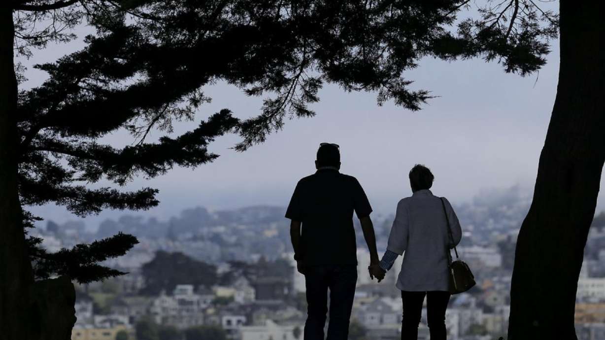 In this July 3, 2017, photo, a man and woman walk under trees down a path at Alta Plaza Park in San Francisco. With inflation pushing up the price of everything from gas to housing to eggs, many retirees are cutting back or eliminating certain costs altogether.