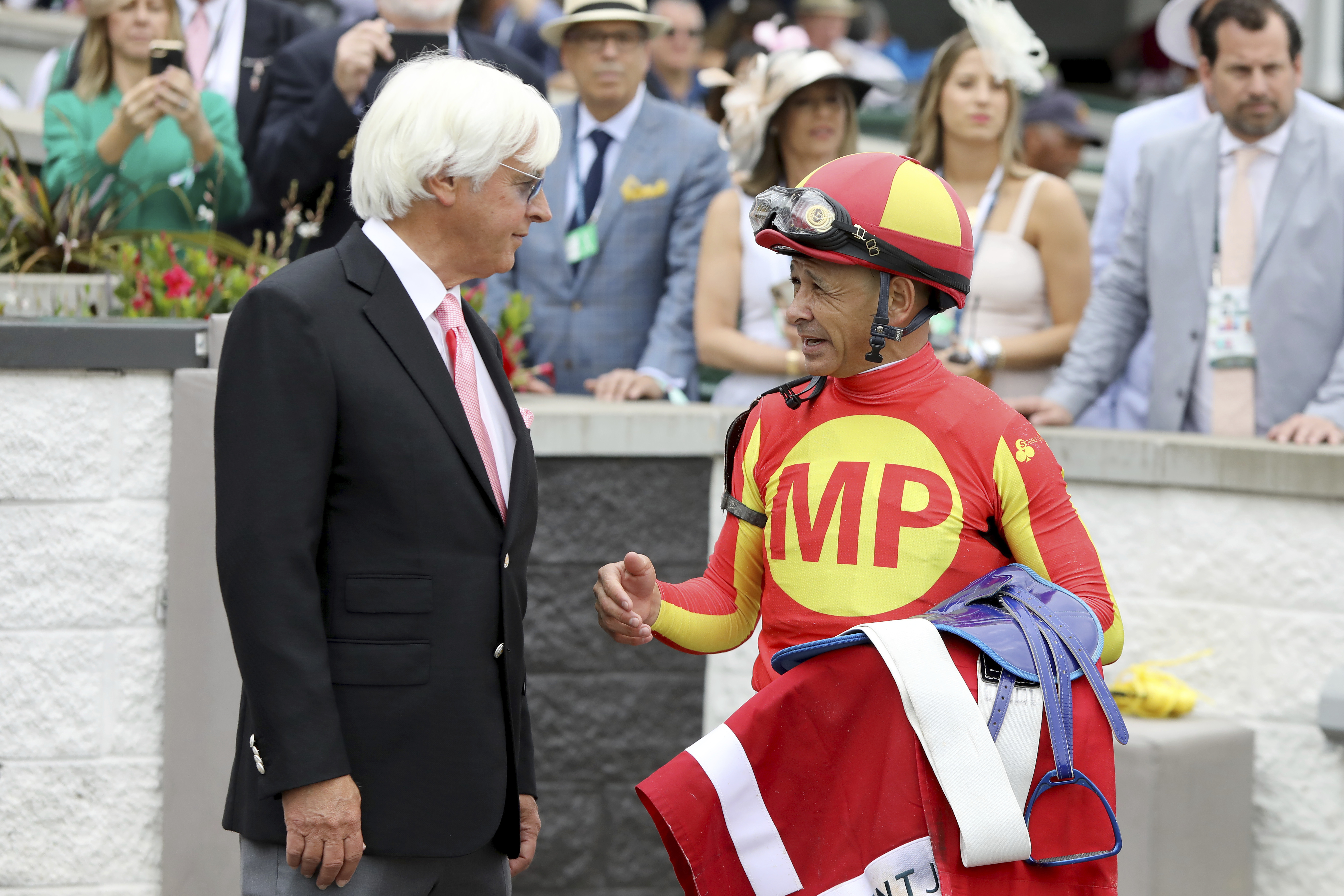 FILE - Jockey Mike Smith talks with trainer Bob Baffert after winning the Grade 2 Alysheba at Churchill Downs, Friday, May 3, 2019, in Louisville, Ky. The Kentucky Derby leads off the first Triple Crown season in decades without the chance of Bob Baffert officially winning one or more of the three races. Baffert's absence while suspended shadows over the race particularly because two horses he trained for a significant period of time are among the top contenders. 