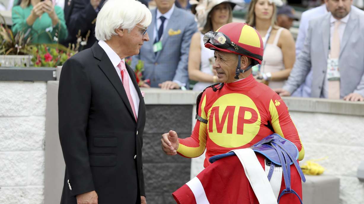 FILE - Jockey Mike Smith talks with trainer Bob Baffert after winning the Grade 2 Alysheba at Churchill Downs, Friday, May 3, 2019, in Louisville, Ky. The Kentucky Derby leads off the first Triple Crown season in decades without the chance of Bob Baffert officially winning one or more of the three races. Baffert's absence while suspended shadows over the race particularly because two horses he trained for a significant period of time are among the top contenders.