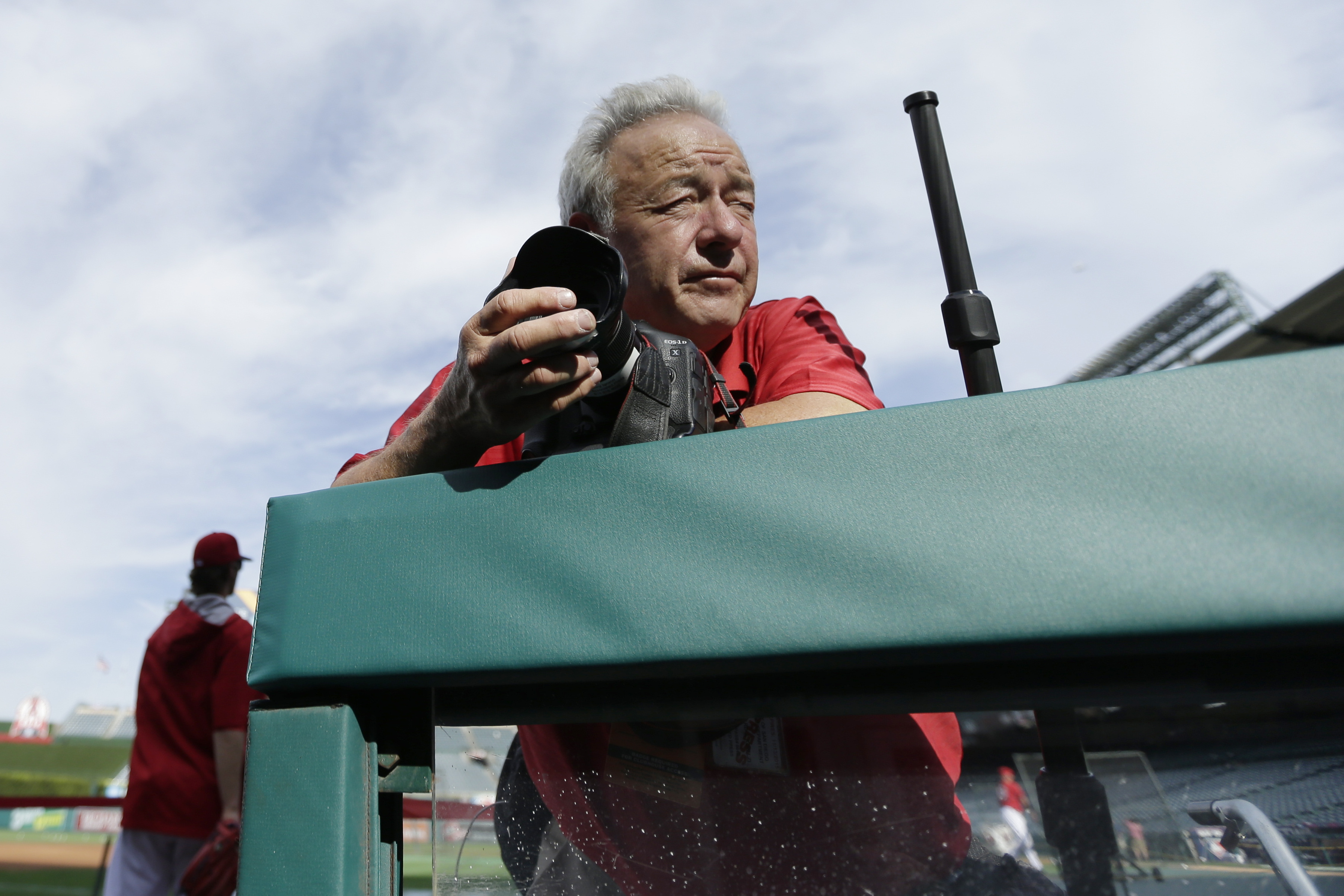 FILE - Photographer Lenny Ignelzi leans against a dugout rail Oct. 3, 2014, before Game 2 of baseball's AL Division Series between the Los Angeles Angels of Anaheim and the Kansas City Royals in Anaheim, Calif. Ignelzi, whose knack for being in the right place at the right time produced breathtaking images of Hall of Fame sports figures, devastating wildfires and other major news over 37 years as photographer for The Associated Press in San Diego, has died. He was 74. Ignelzi died Friday, April 29, 2022, in Las Vegas of cerebral amyloid angiopathy, a brain condition that triggers frequent strokes, according to his wife, Bobbi. 