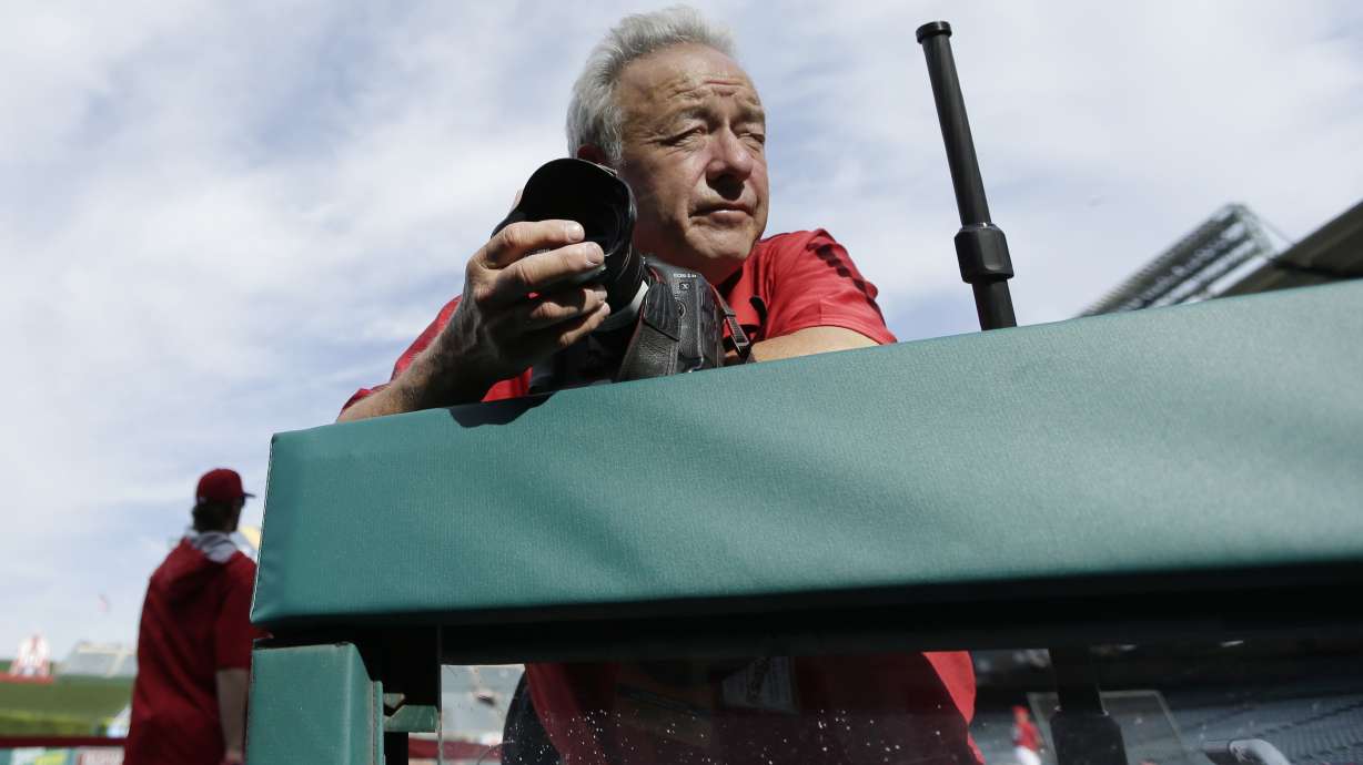FILE - Photographer Lenny Ignelzi leans against a dugout rail Oct. 3, 2014, before Game 2 of baseball's AL Division Series between the Los Angeles Angels of Anaheim and the Kansas City Royals in Anaheim, Calif. Ignelzi, whose knack for being in the right place at the right time produced breathtaking images of Hall of Fame sports figures, devastating wildfires and other major news over 37 years as photographer for The Associated Press in San Diego, has died. He was 74. Ignelzi died Friday, April 29, 2022, in Las Vegas of cerebral amyloid angiopathy, a brain condition that triggers frequent strokes, according to his wife, Bobbi.
