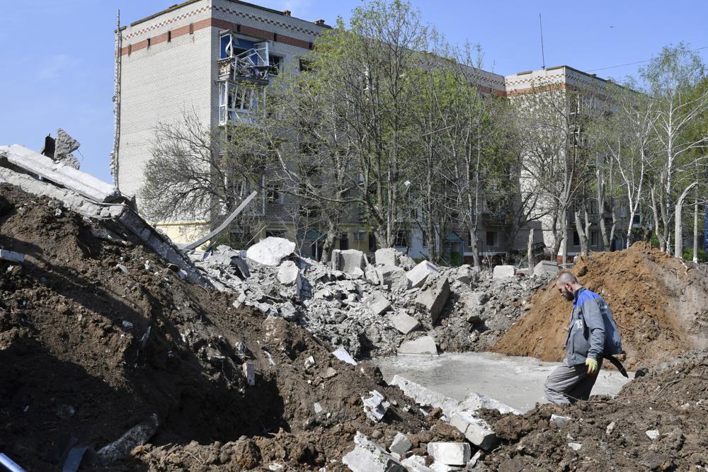 A worker stands next to a crater of an explosion next to an apartment building damaged by night shelling in Kramatorsk, Ukraine, Thursday. Heavy fighting raged Thursday at the shattered steel plant in Mariupol as Russian forces attempted to finish off the city's last-ditch defenders.