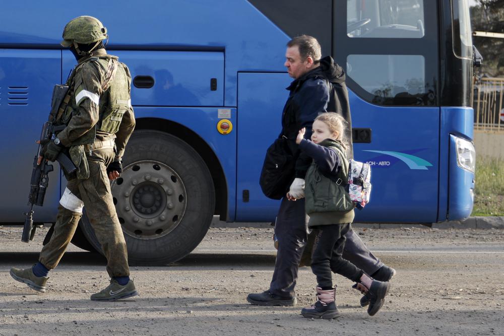 A man and a girl who left a shelter in the Metallurgical Combine Azovstal walk to a bus escorted by a serviceman of the Russian Army in Mariupol, in territory under the government of the Donetsk People's Republic, eastern Ukraine, Friday.