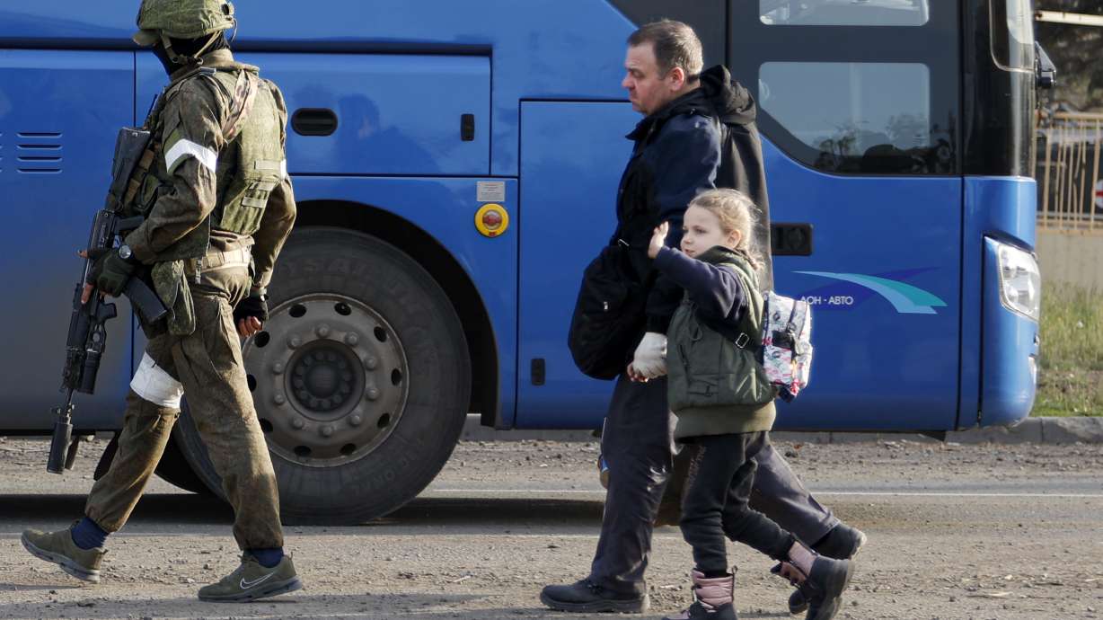 A man and a girl who left a shelter in the Metallurgical Combine Azovstal walk to a bus escorting by a serviceman of Russian Army in Mariupol, in territory under the government of the Donetsk People's Republic, eastern Ukraine, Friday.