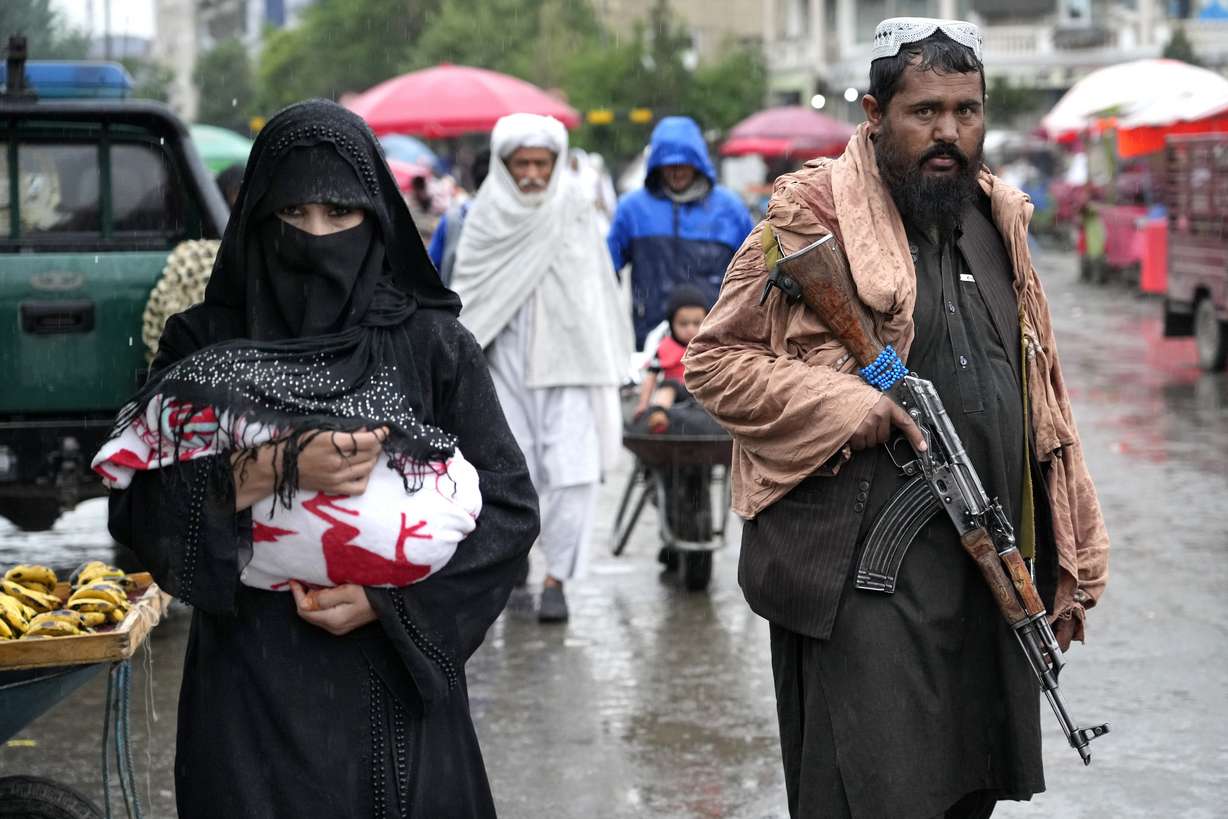 An Afghan woman walks through the old market as a Taliban fighter stands guard, in downtown Kabul, Afghanistan, Tuesday. Afghanistan’s Taliban rulers on Saturday ordered all Afghan women to wear head-to-toe clothing in public, a sharp hard-line pivot that confirmed the worst fears of rights activists and was bound to further complicate Taliban dealings with an already distrustful international community.