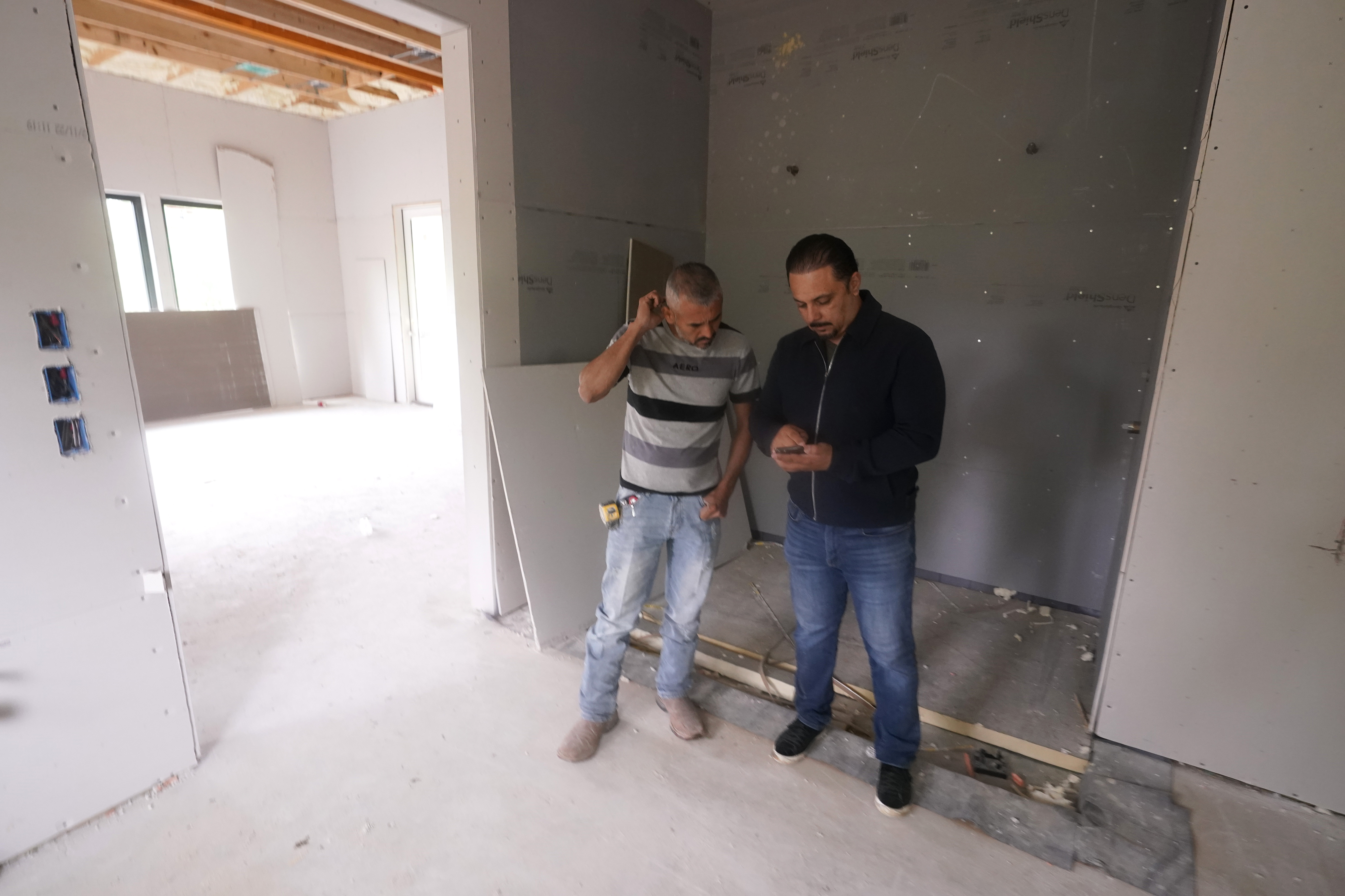 Tile subcontractor Horacio Gomez, originally from the Mexican state of Michoacan, confers with homebuilder Joshua Correa about plans at a custom home under construction in Plano, Texas, Tuesday. There are an estimated 2 million fewer immigrants than expected in the United States, helping fuel a desperate scramble for workers in many sectors, from meatpacking to homebuilding, that is also contributing to shortages and price increases.
