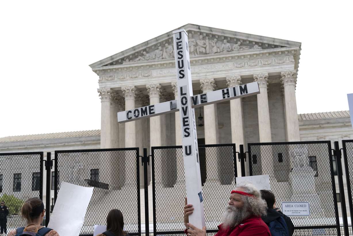 A demonstrator holding a cross protests outside of the US Supreme Court, Thursday, in Washington. America's faithful are bracing, some with cautionary joy and others with looming dread, for the Supreme Court to potentially overturn the landmark 1973 Roe v. Wade decision and end the nationwide right to legal abortion.
