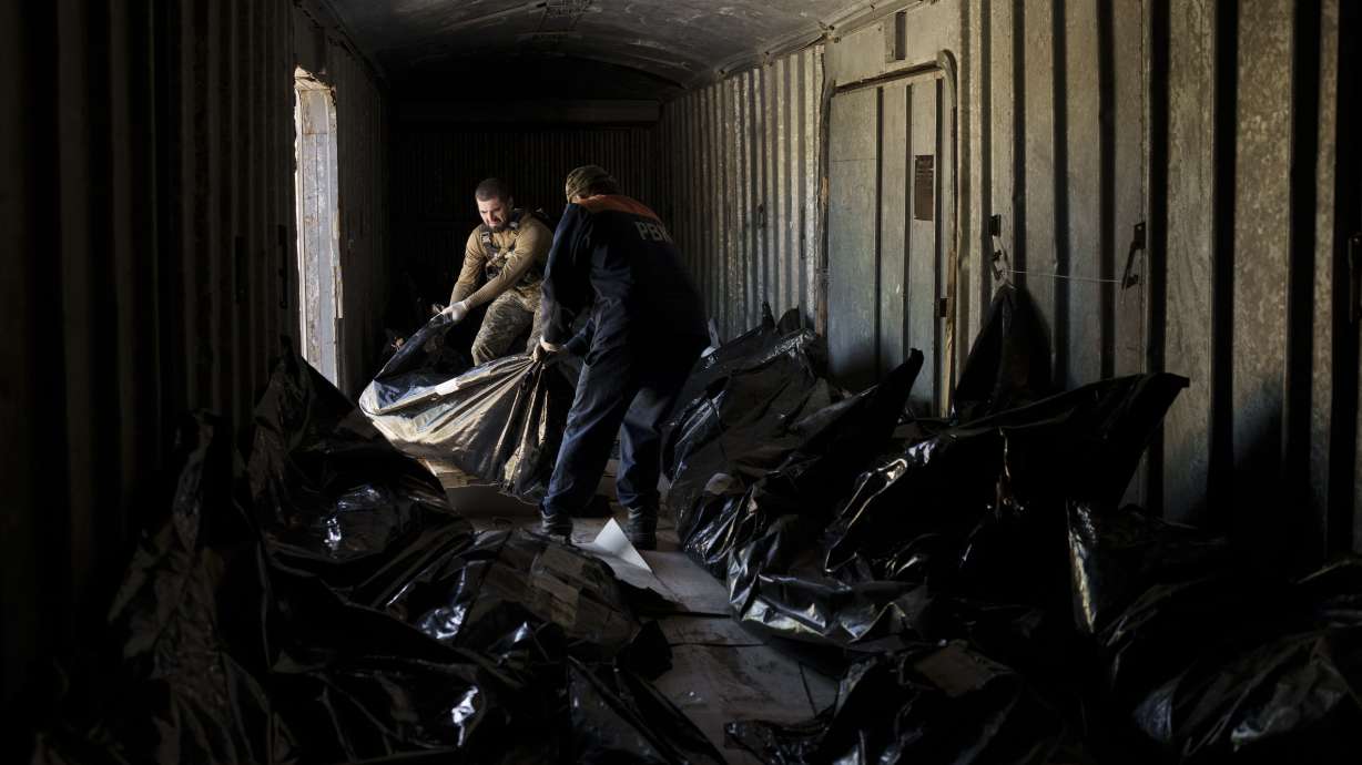 A Ukrainian serviceman and a worker carry the body of a Russian soldier into a refrigerated train in Kharkiv, Ukraine, Thursday. The bodies of more than 40 Russian soldiers who were found after battles around Kharkiv are being stored in the refrigerated car. Russian President Vladimir Putin marked his country's biggest patriotic holiday Monday without a major new battlefield success in Ukraine.