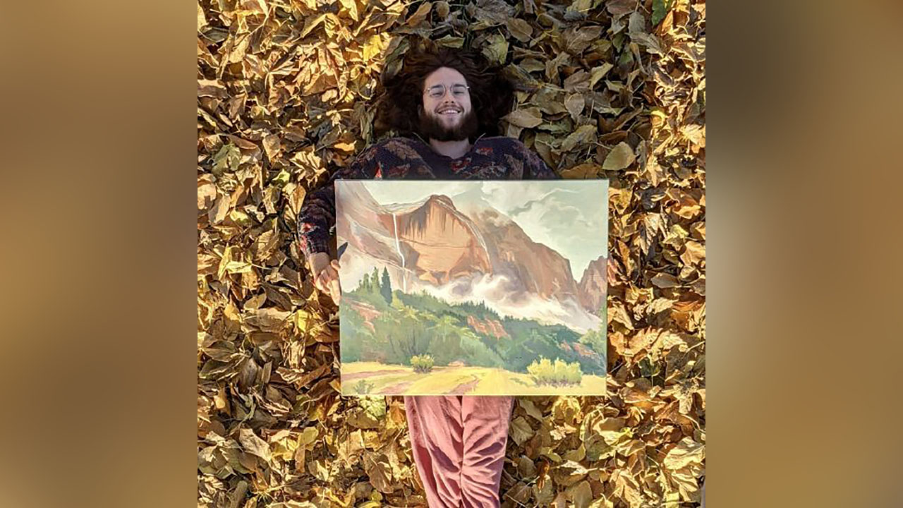 Artist Steven Anzardo lies on fall leaves holding one of his paintings. Anzardo traveled the country in his SUV painting landscapes.