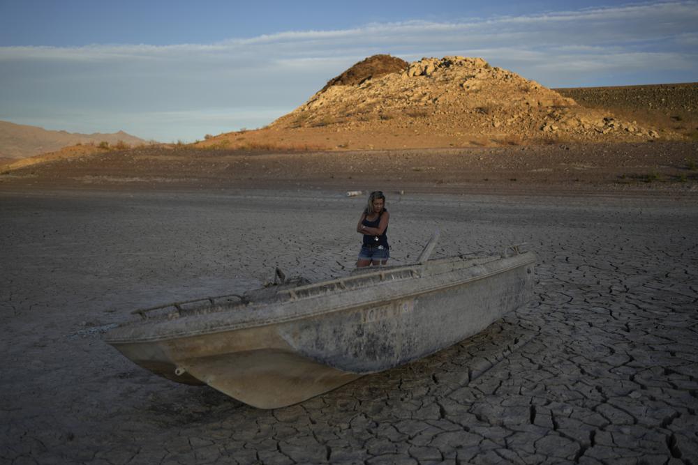 Misha McBride looks at a formally sunken boat now on cracked earth hundreds of feet from what is now the shoreline on Lake Mead at the Lake Mead National Recreation Area, Monday, near Boulder City, Nev.