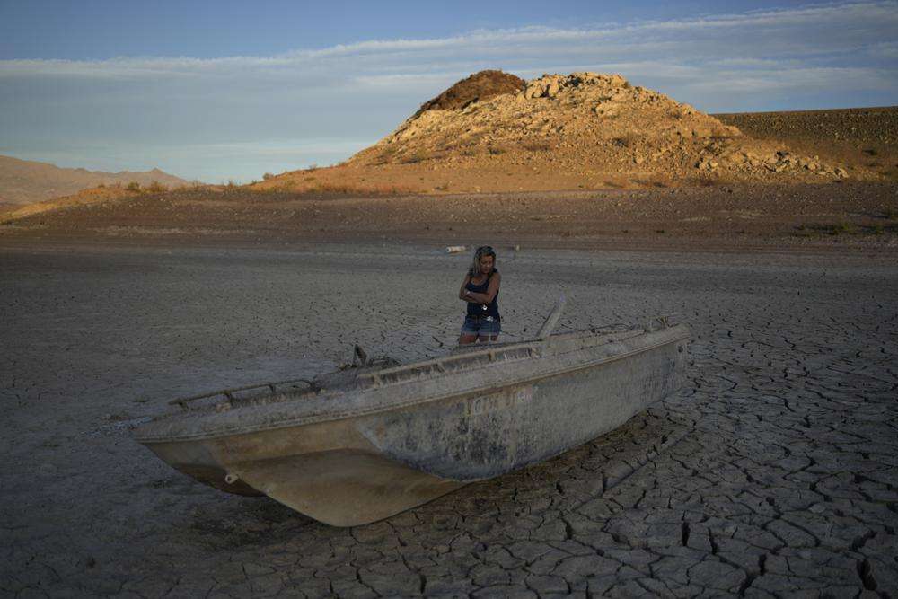 Misha McBride looks at a formally sunken boat now on cracked earth hundreds of feet from what is now the shoreline on Lake Mead at the Lake Mead National Recreation Area, Monday, near Boulder City, Nev.