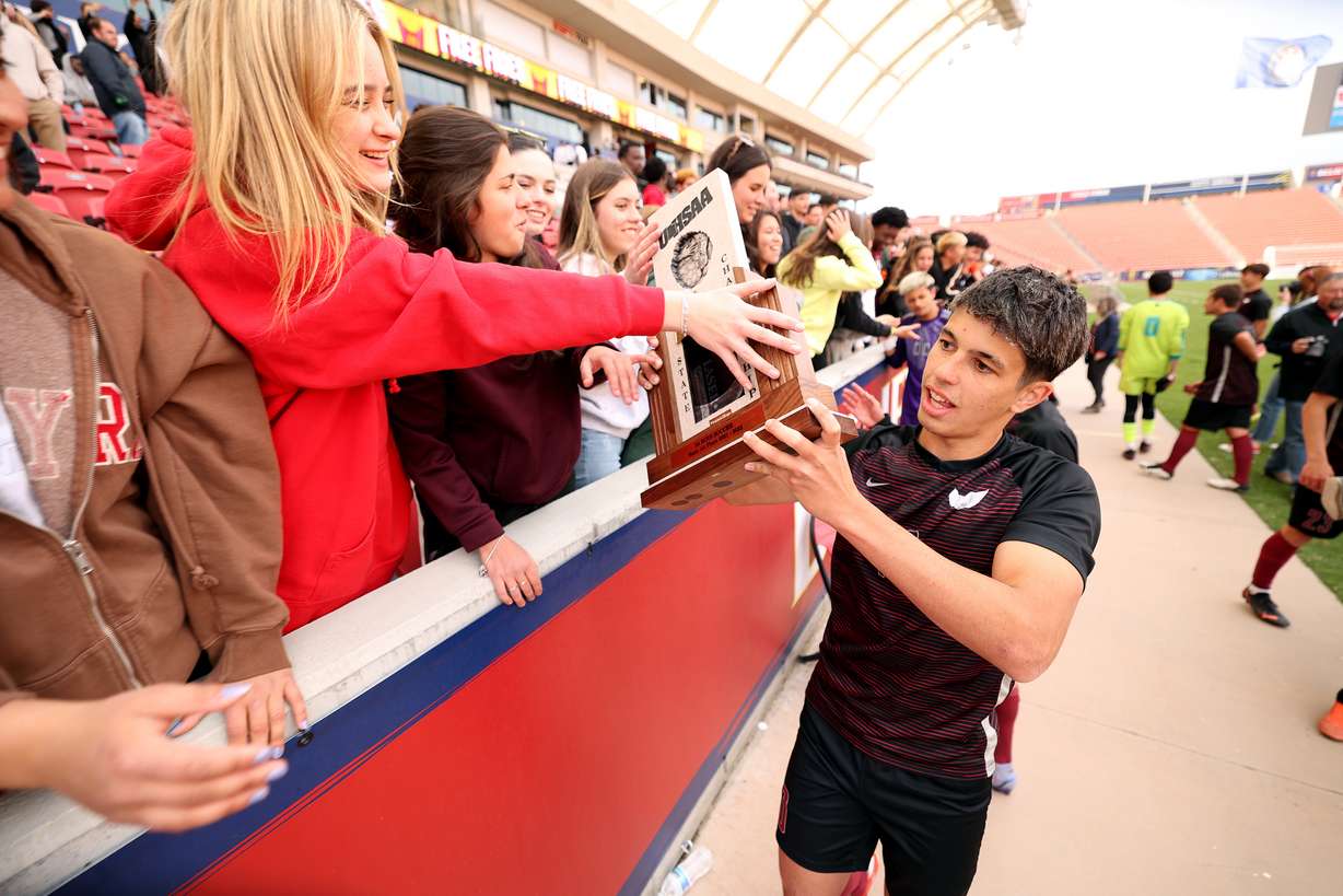 Layton Christian Academy’s Enzo Jaques, who scored three goals, carries the championship trophy past the students after the game with Real Salt Academy in the 3A boys state soccer championship at Rio Tinto Stadium in Sandy on Wednesday, May 11, 2022. Layton Christian Academy won 4-0.