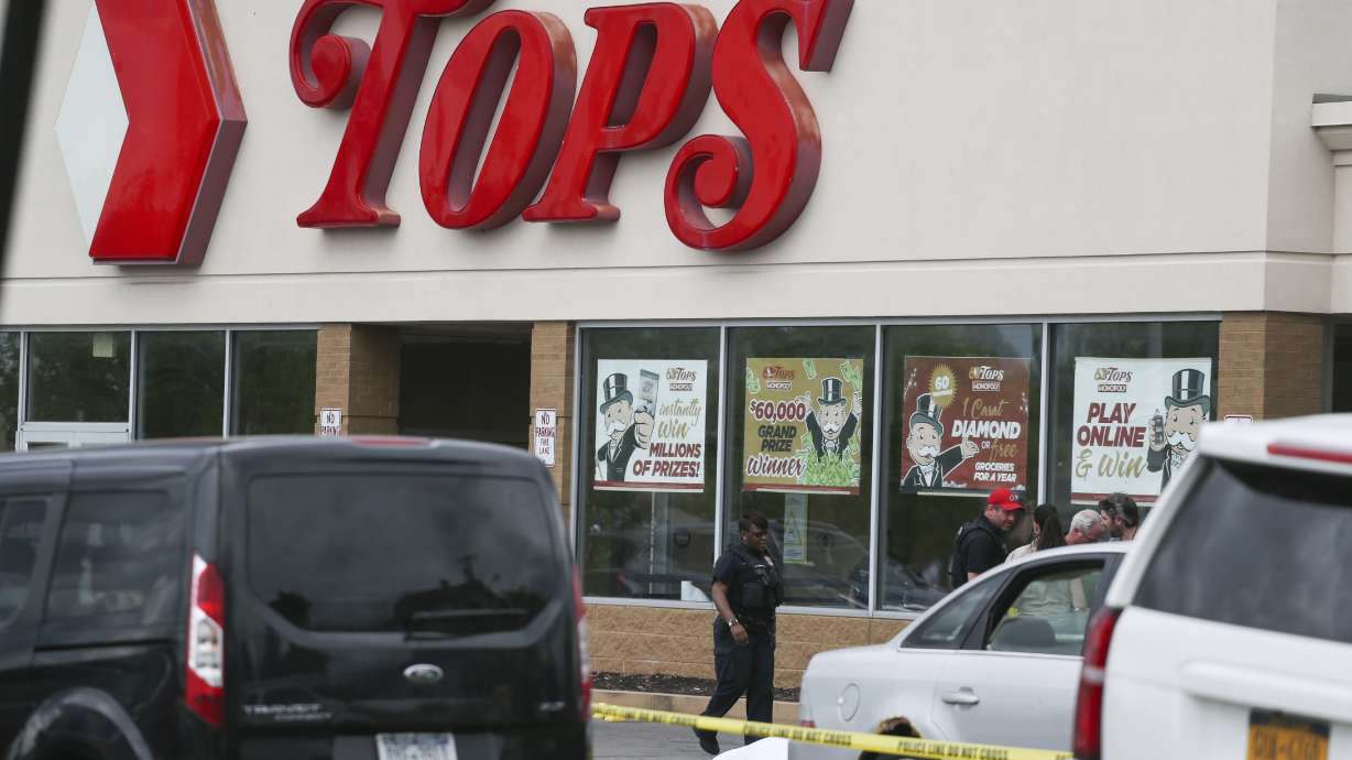 A crowd gathers as police investigate after a shooting at a supermarket on Saturday, in Buffalo, N.Y. Multiple people were shot at the Tops Friendly Market. Police have notified the public that the alleged shooter was in custody.
