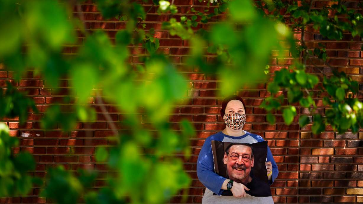 Sara Atkins poses for a photo, in Wynnewood, Pa., Tuesday while holding a pillow with an image of her father Andy Rotman-Zaid, who died of COVID-19 in December 2020. The U.S. death toll from COVID-19 has hit 1 million Monday, less than 2 1/2 years into the outbreak.