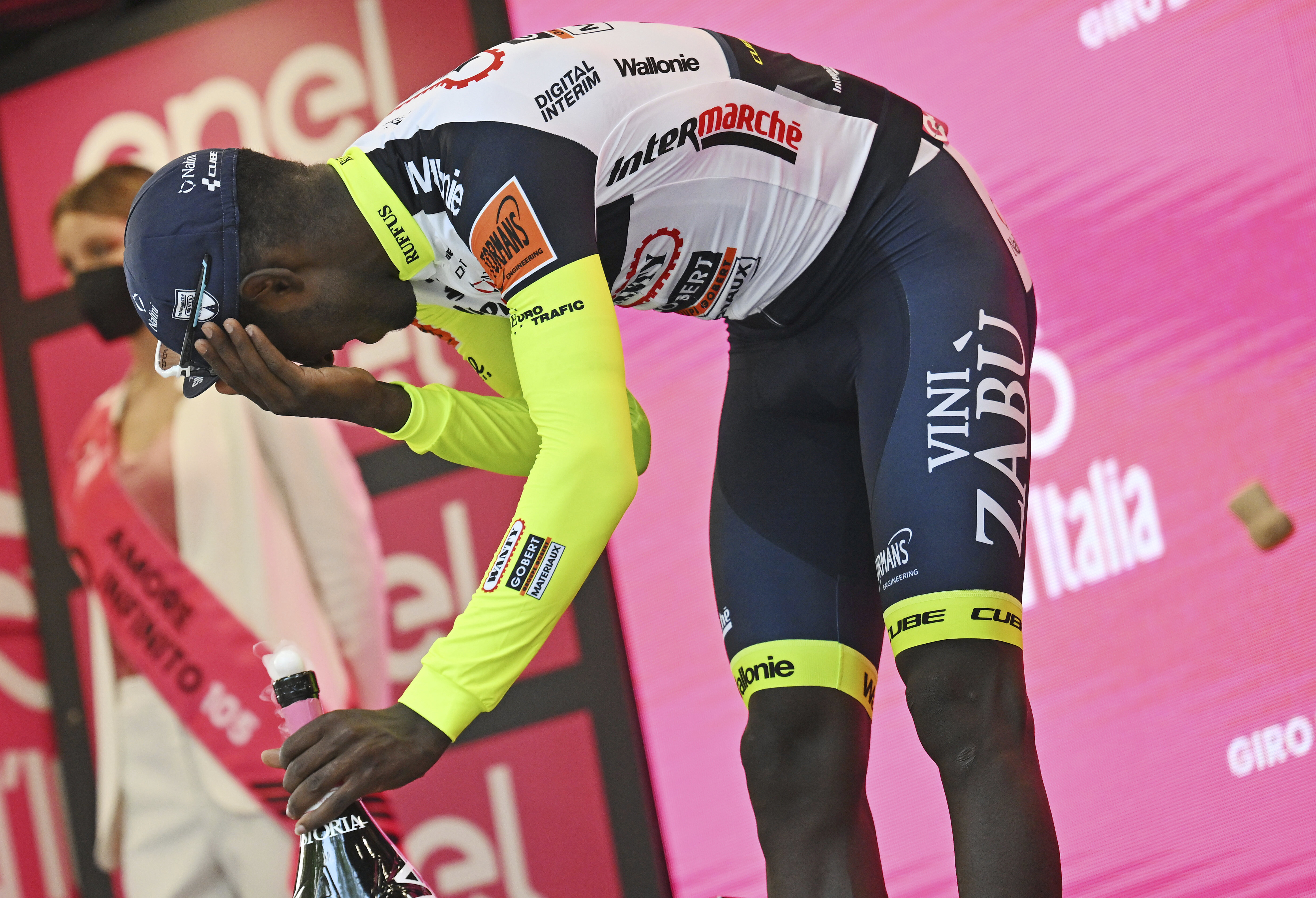 Eritrea's Biniam Girmay touches his eye after spraying sparkling wine on the podium to celebrate winning the 10th stage of the Giro D'Italia cycling race from Pescara to Jesi, Italy, Tuesday, May 17, 2022. Girmay was then taken to a local hospital after getting injured when he popped a champagne cork into his eye during the podium celebration.