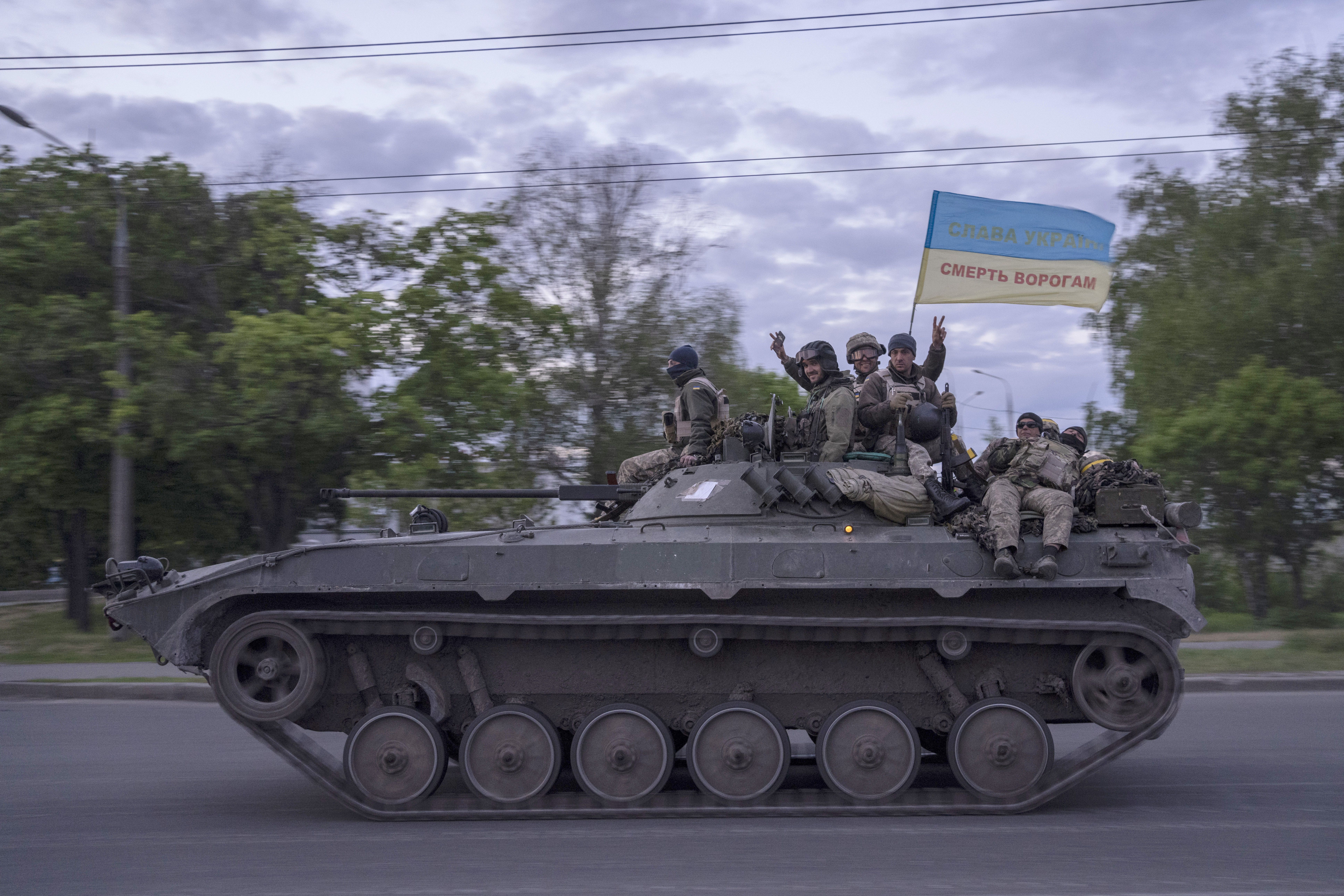 Ukrainian serviceman wave a flag with writing reading in Ukrainian “Glory to Ukraine,” top, and “Death to the enemies” as they ride atop a tank in the Kharkiv region, eastern Ukraine, on Monday.