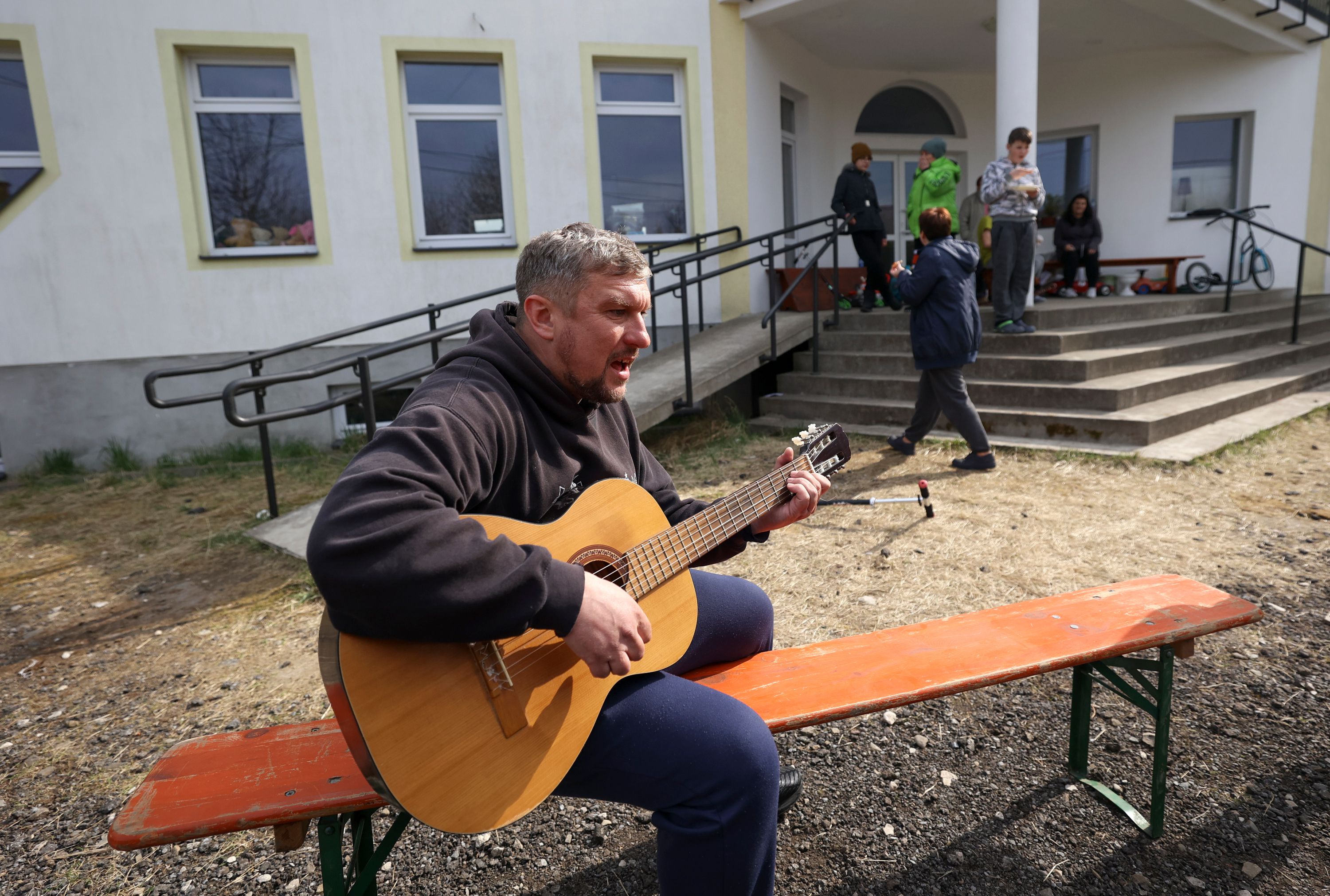 Ukrainian refugee Sergey Kuzmenko, from the Bucha region, plays guitar for other refugees and volunteers outside of a large home used to house about 80 refugees in Rzeszow, Poland, on April 19.