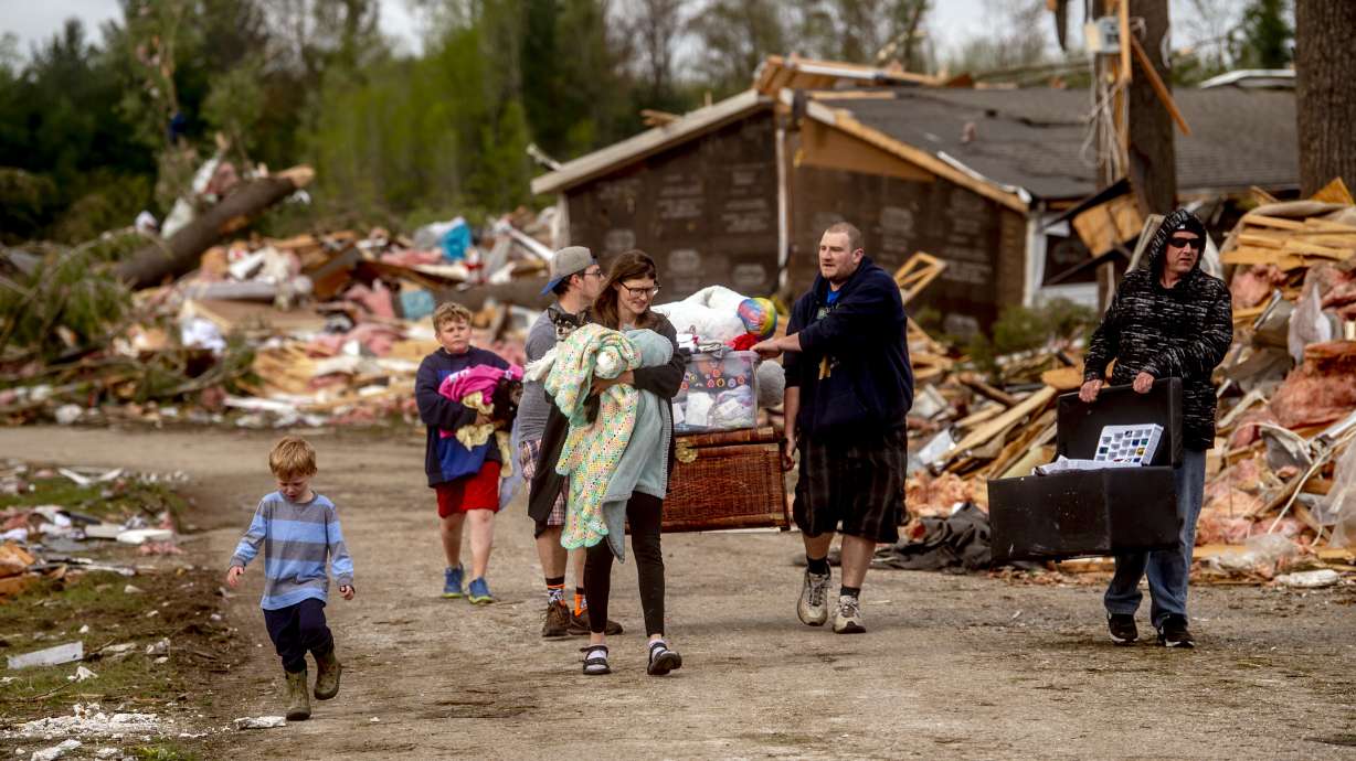 Resident Stephanie Kerwin, center, holds her baby Octavius in one arm and dog Pixie in the other as she and her family carry what they could salvage from her home in Nottingham Forest Mobile Home Park, Saturday, in Gaylord, Mich., following a tornado the day before.