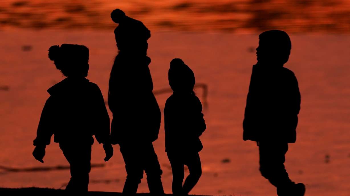 Kids are silhouetted against a pond at a park in Lenexa, Kan., on Dec. 26, 2020. Health officials remain perplexed by mysterious cases of severe liver damage in hundreds of young children around the world.