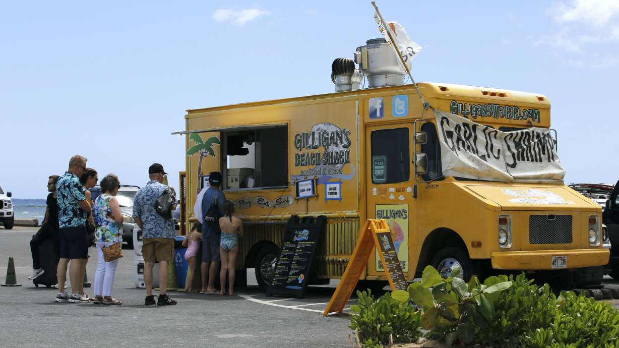People line up at a food truck parked near Waikiki Beach in Honolulu, Monday. A COVID surge is underway that is starting to cause disruptions as schools wrap up for the year and Americans prepare for summer vacations.