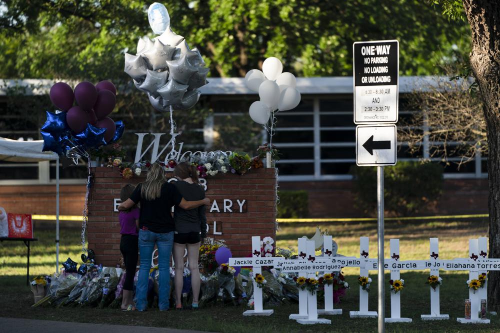 A family pays their respects next to crosses bearing the names of Tuesday's shooting victims at Robb Elementary School in Uvalde, Texas, Thursday. The gunman who massacred 19 children and two teachers at a Texas elementary school was inside for more than an hour before he was killed in a shootout, law enforcement authorities said Thursday.
