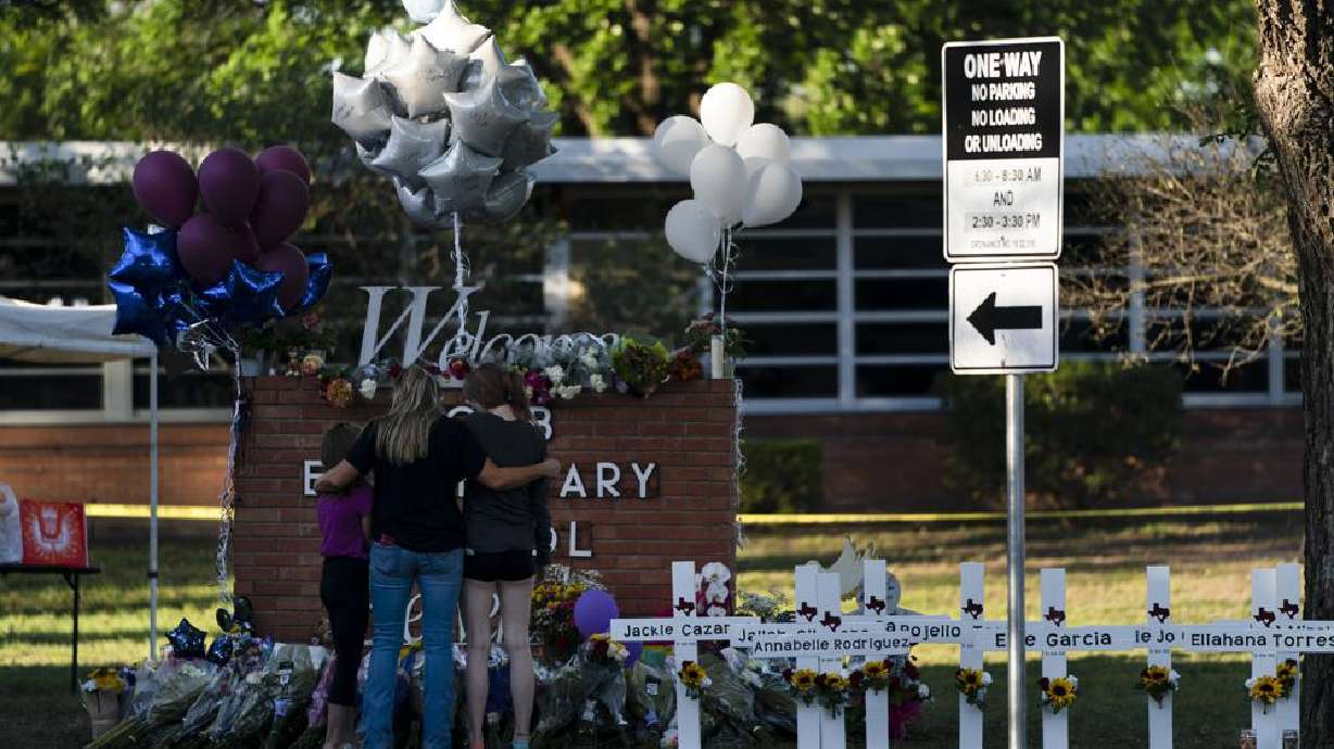 A family pays their respects next to crosses bearing the names of Tuesday's shooting victims at Robb Elementary School in Uvalde, Texas, Thursday. The gunman who massacred 19 children and two teachers at a Texas elementary school was inside for more than an hour before he was killed in a shootout, law enforcement authorities said Thursday.