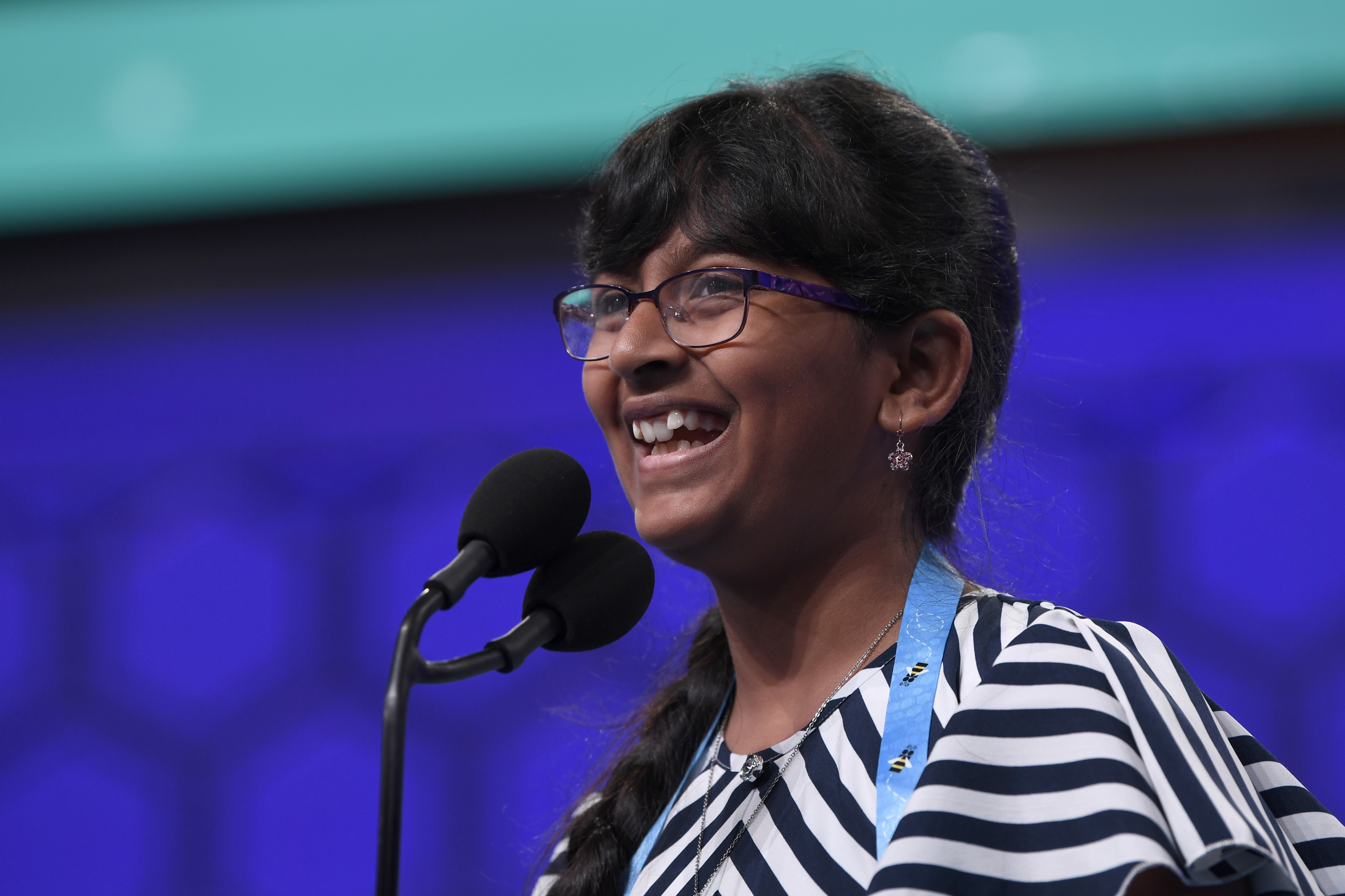 FILE - Harini Logan, 11, of San Antonio, smiles after correctly spelling her word as she competes in the finals of the Scripps National Spelling Bee in Oxon Hill, Md., Thursday, May 30, 2019. The Scripps National Spelling Bee is back, fully in person at its usual venue outside Washington for the first time since 2019. But the pandemic continues to affect kids who've spent years preparing to compete for spelling's top prize.  