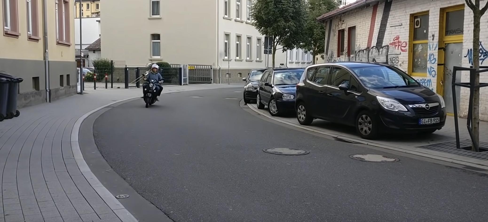 The "muffler" noise connected to this electric moped is being produced by the passenger with a good ol' fashioned, marching band elite trombone.