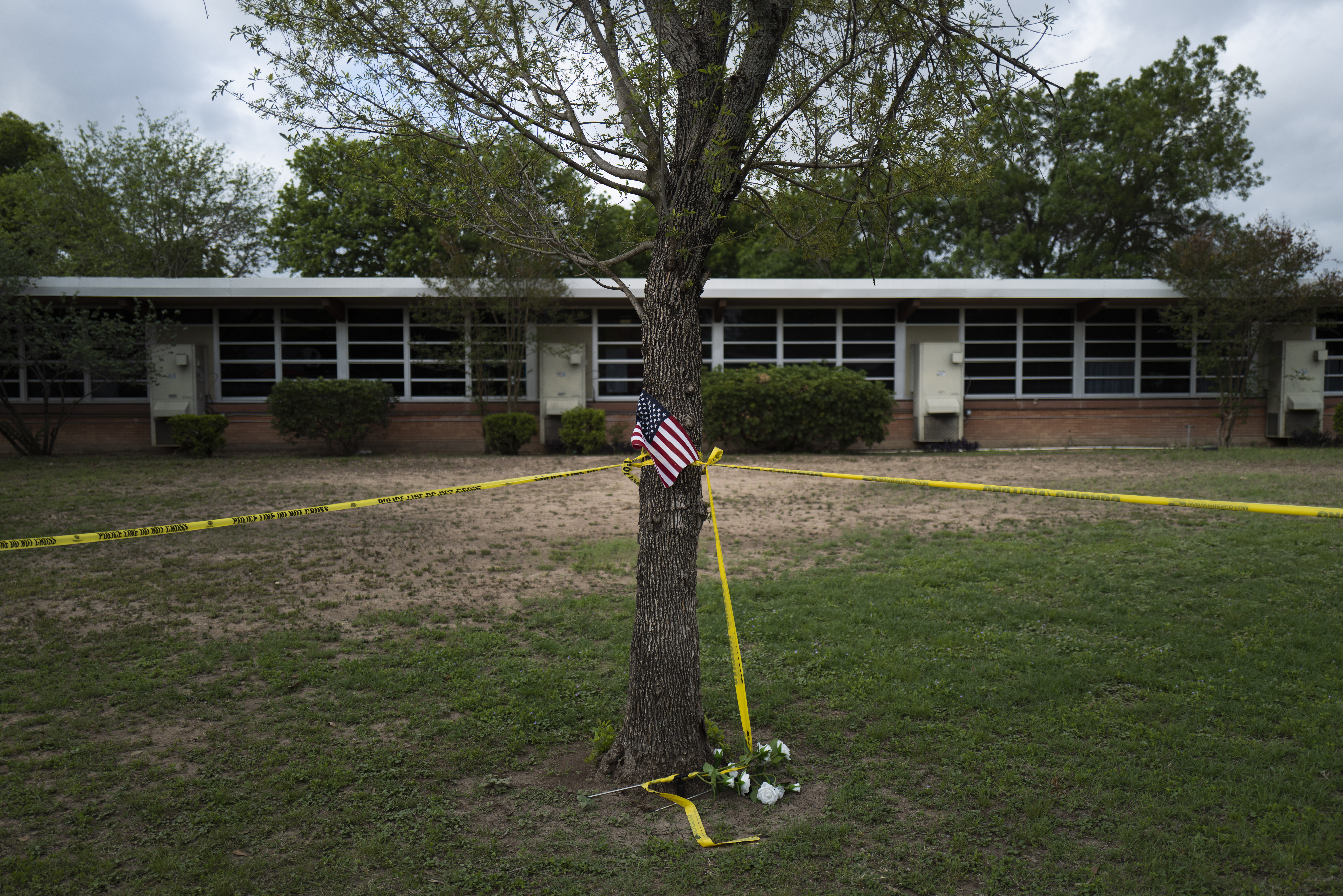 A school building stands behind a tree with an American flag and crime scene tape at Robb Elementary School in Uvalde, Texas, Monday. On May 24, an 18-year-old entered the school and fatally shot several children and teachers. 